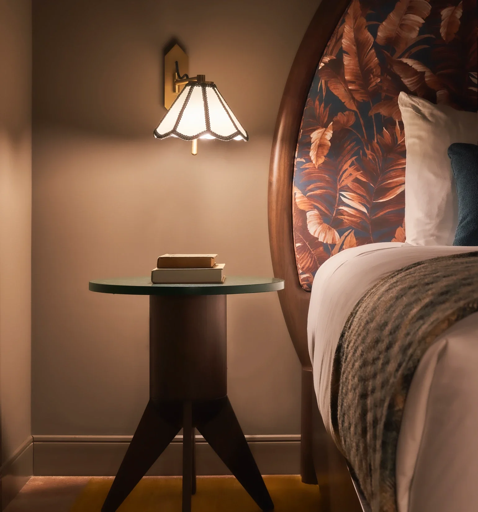 Lampe de chevet allumée à côté d'un lit avec un oreiller blanc et une couverture brune, dans une chambre chaleureuse