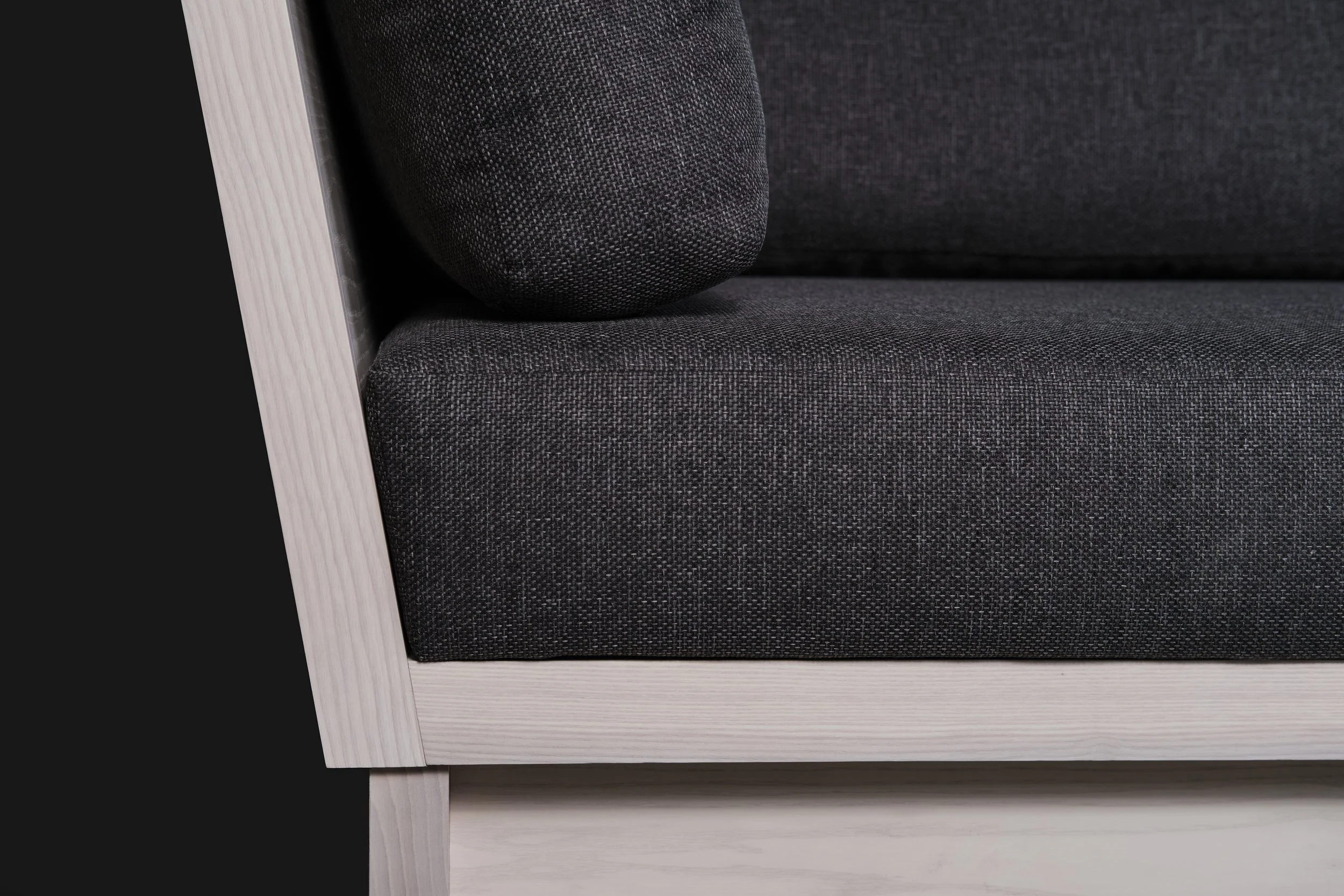 Détail d'un canapé moderne avec structure en bois clair et assise en tissu gris foncé.