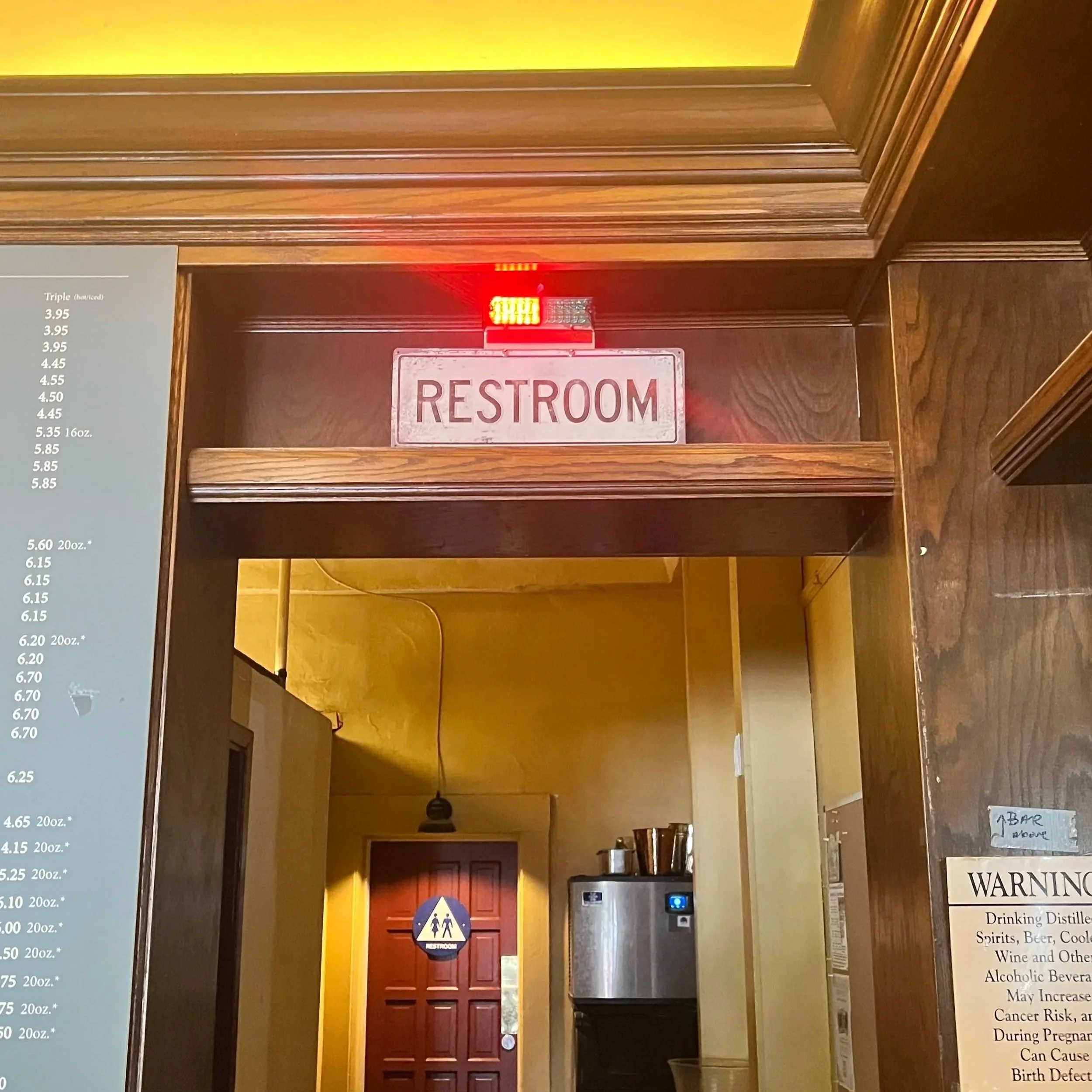 An indoor view of a restaurant's restroom entrance, with a sign that says 'RESTROOM' above the door, and a red illuminated emergency light above the sign.