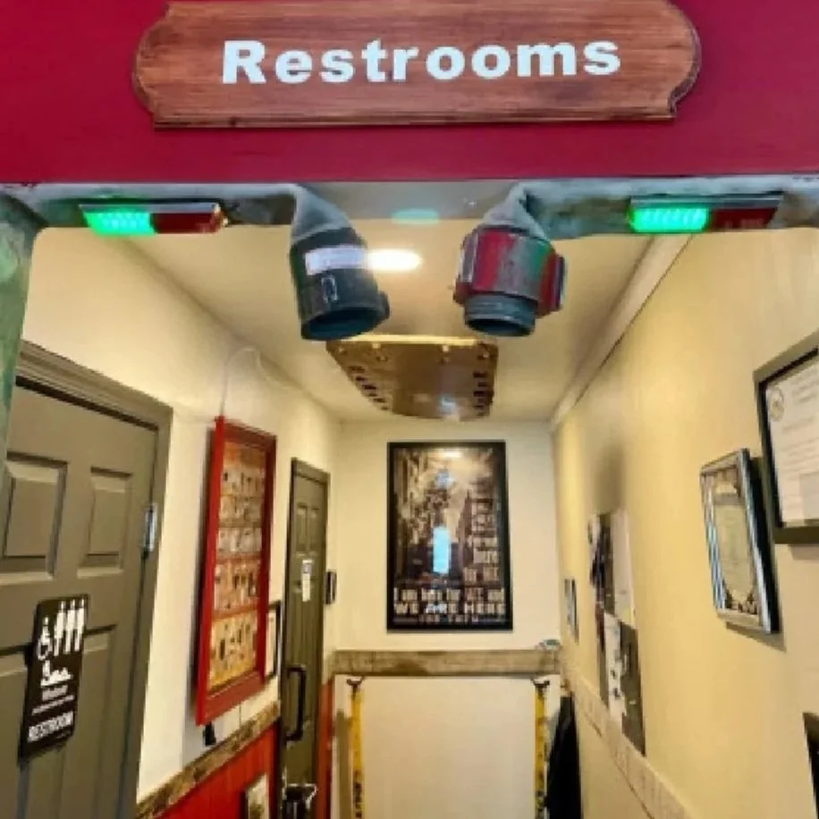 Hallway near restroom with a wooden sign labeled 'Restrooms' hanging above the entrance, and security cameras mounted on the ceiling.