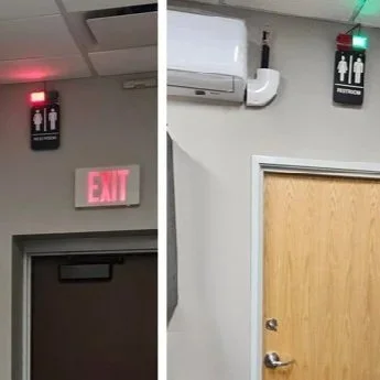 A split image showing two restroom signs on adjacent walls; the left side has a black sign with a red light above it indicating men's restroom, and the right side has a black sign with a green light above it indicating women's restroom.