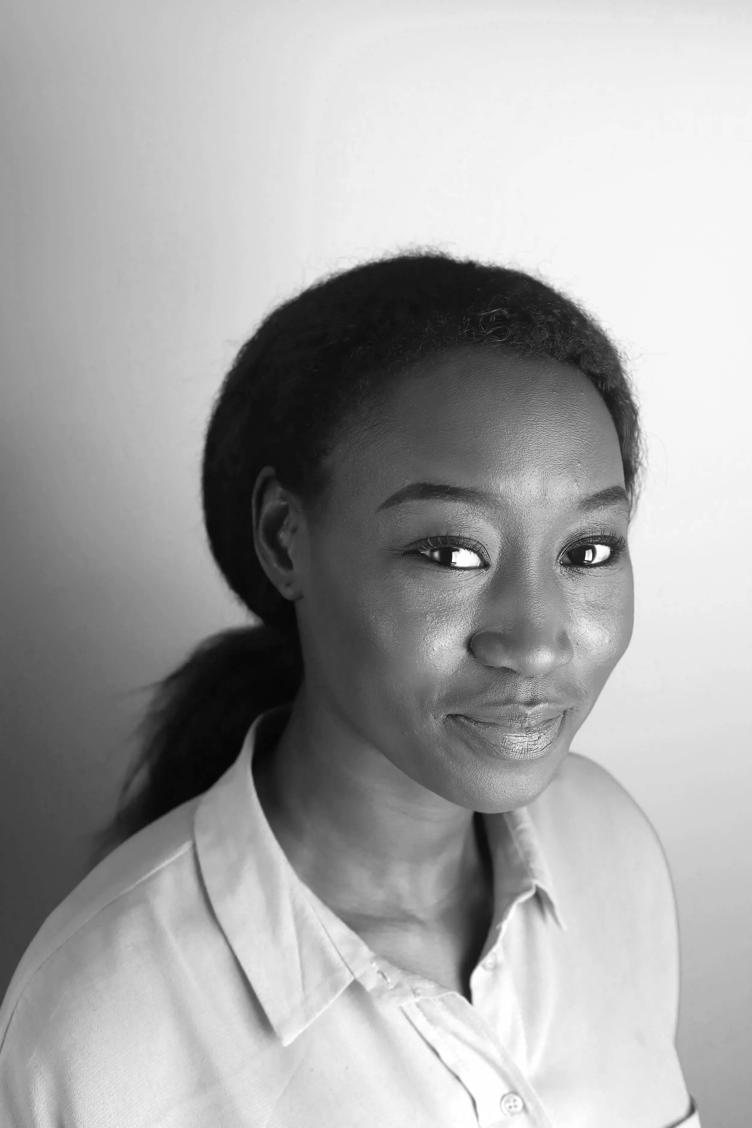 Black and white portrait of a woman with dark hair pulled back, wearing a light-colored collared shirt, smiling softly at the camera.