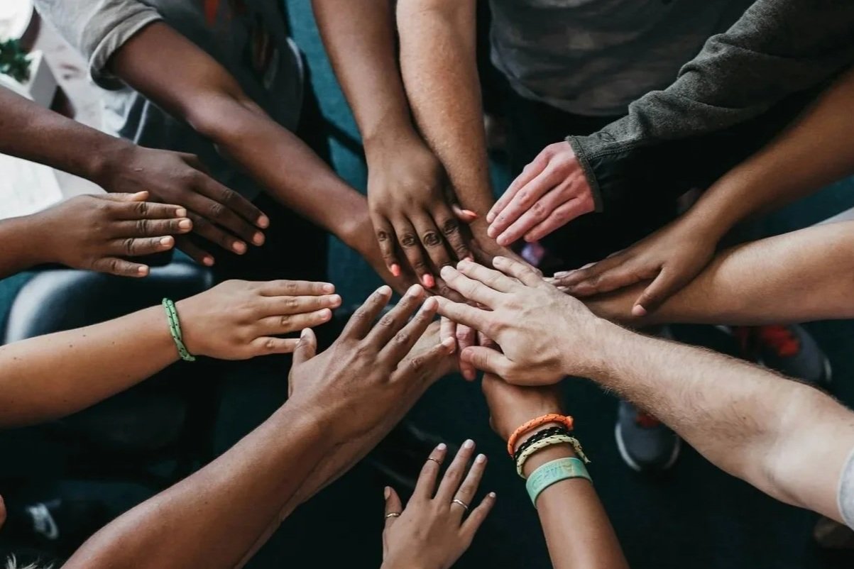 Group of diverse hands stacked together in the center, symbolizing unity and teamwork.