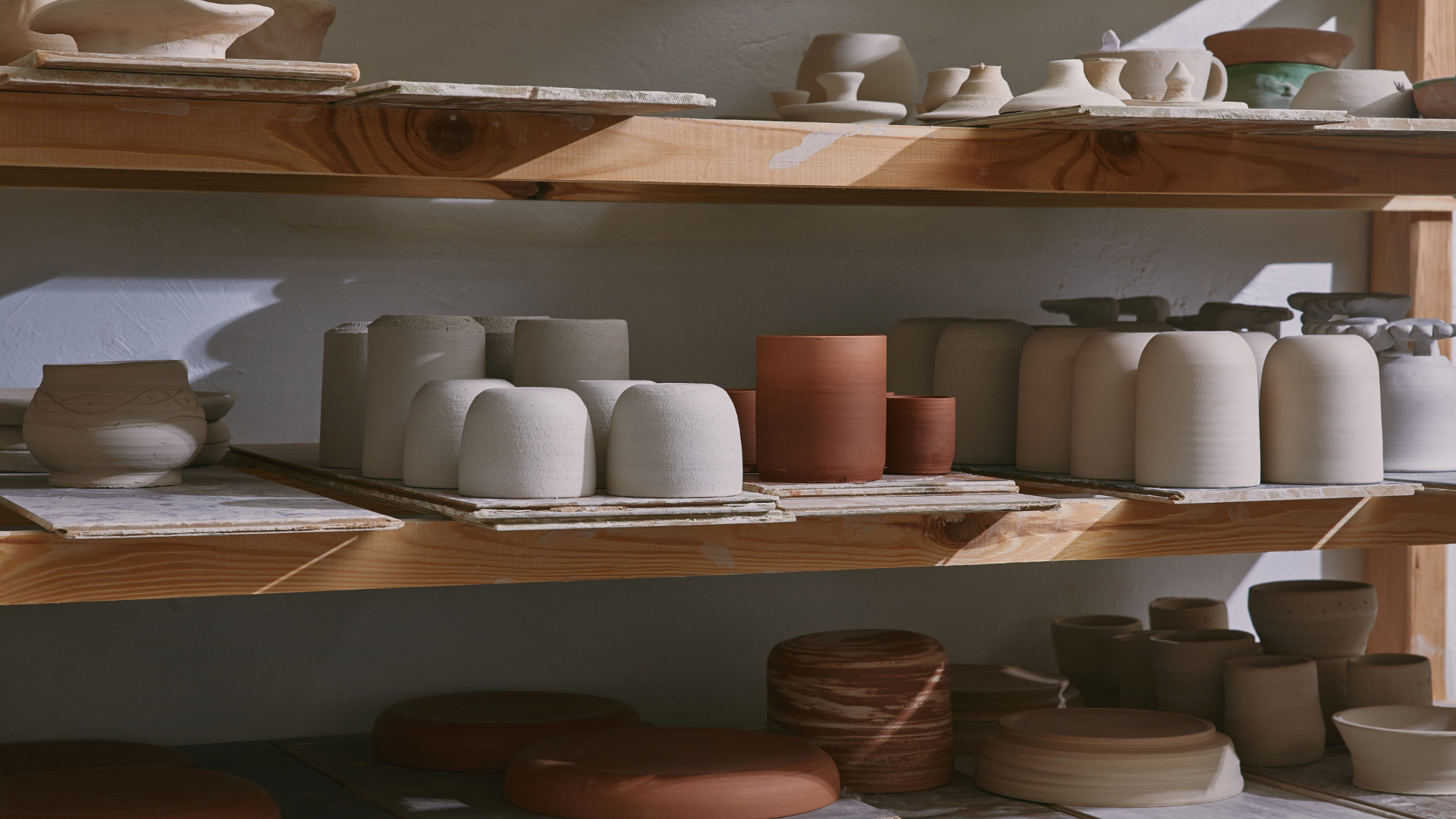 Shelving with handmade pottery pieces and ceramics inside a pottery studio work space.