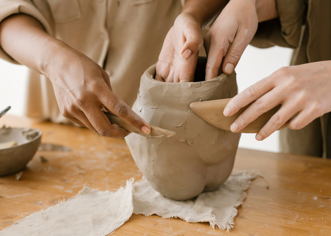 Hands building and shaping a clay vessel during a collaborative pottery workshop.
