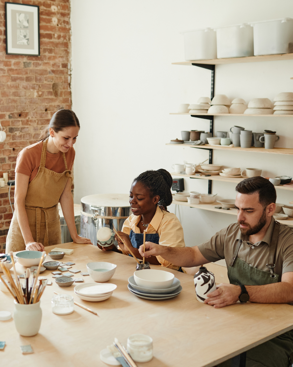Pottery workshop with people glazing ceramics in a warm studio space.
