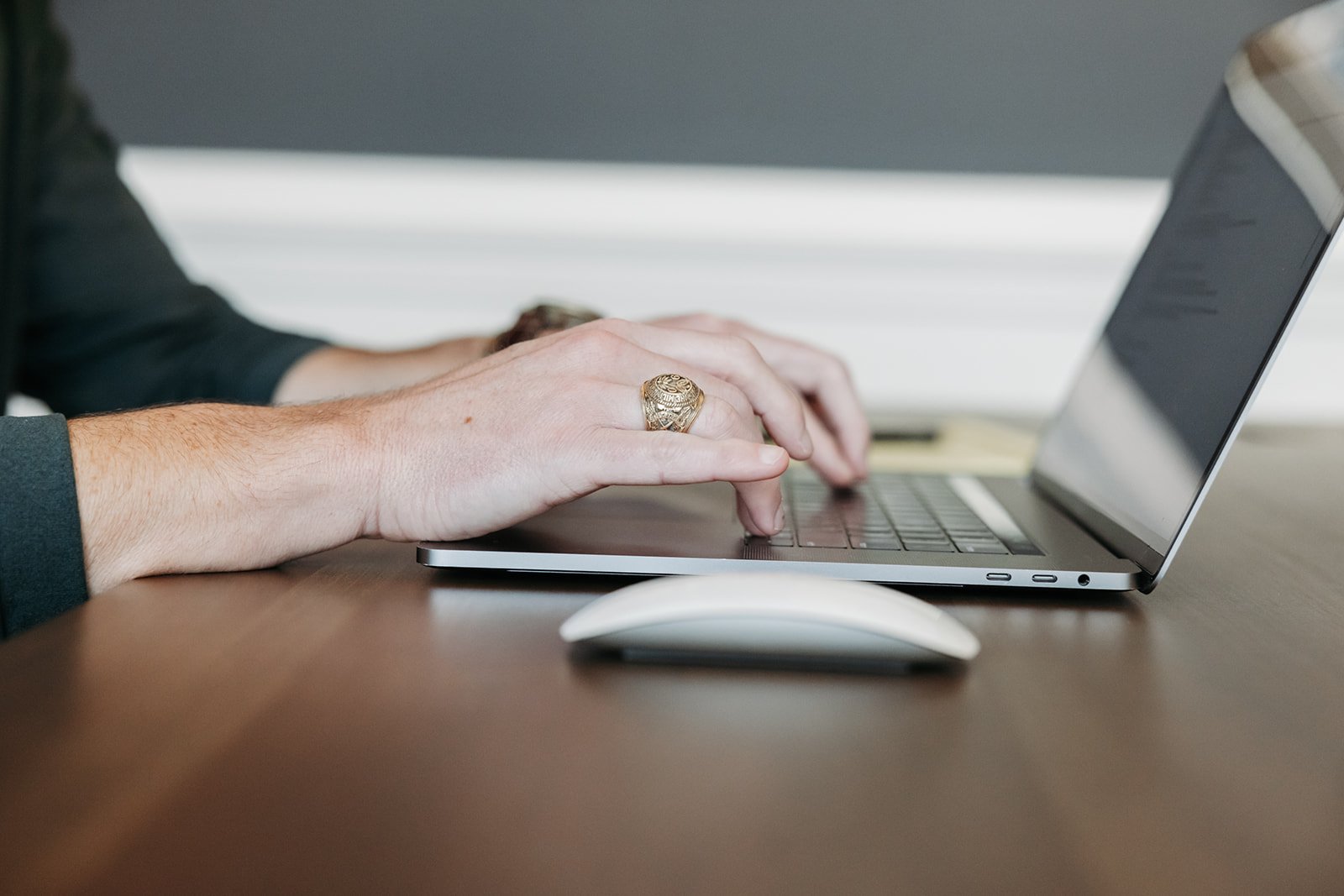 Person typing on a laptop computer at a wooden desk with a white mouse nearby.