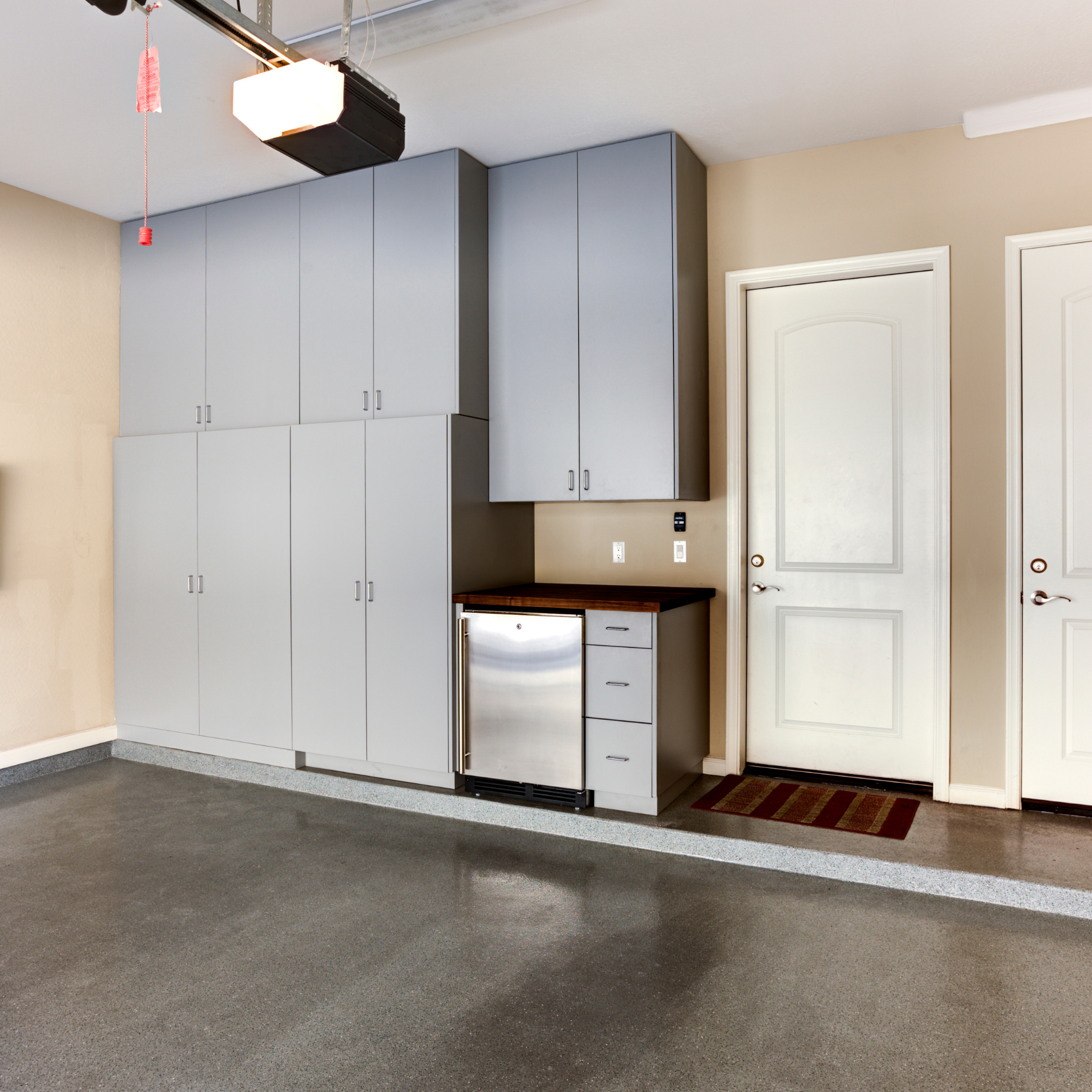 Organized garage setup featuring tall gray storage cabinets, a wood countertop, a stainless steel mini fridge, and polished epoxy flooring.