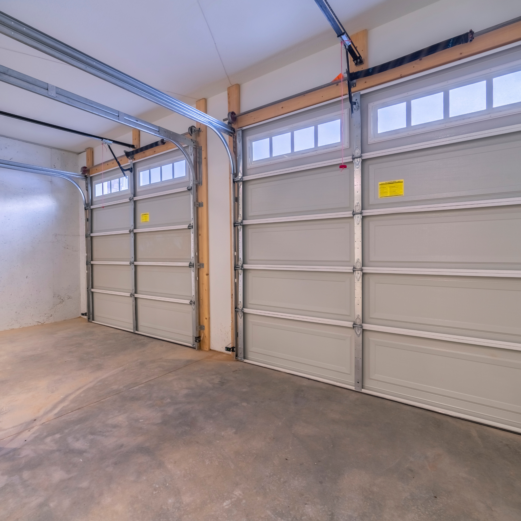 Clean, empty garage with closed beige garage doors and a bare concrete floor.