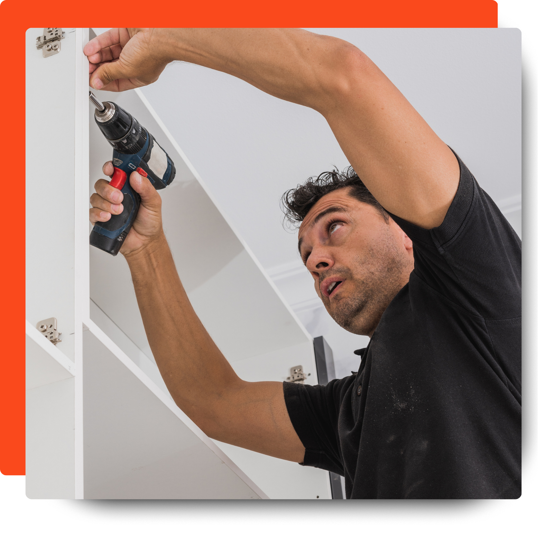 Man installing cabinetry using a power drill, securing hardware inside a white cabinet frame.