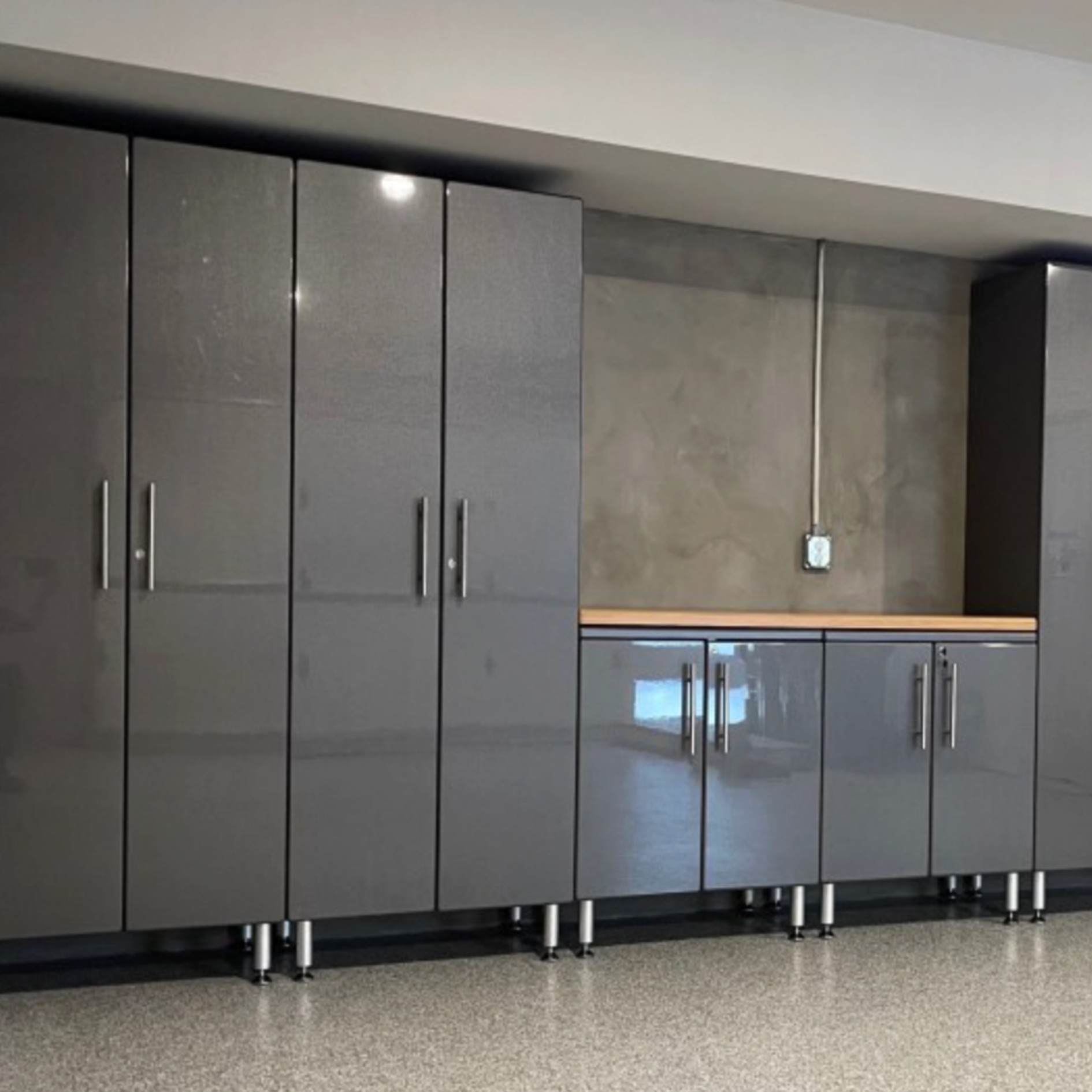 Modern garage with glossy gray storage cabinets and a wood countertop installed along the wall.
