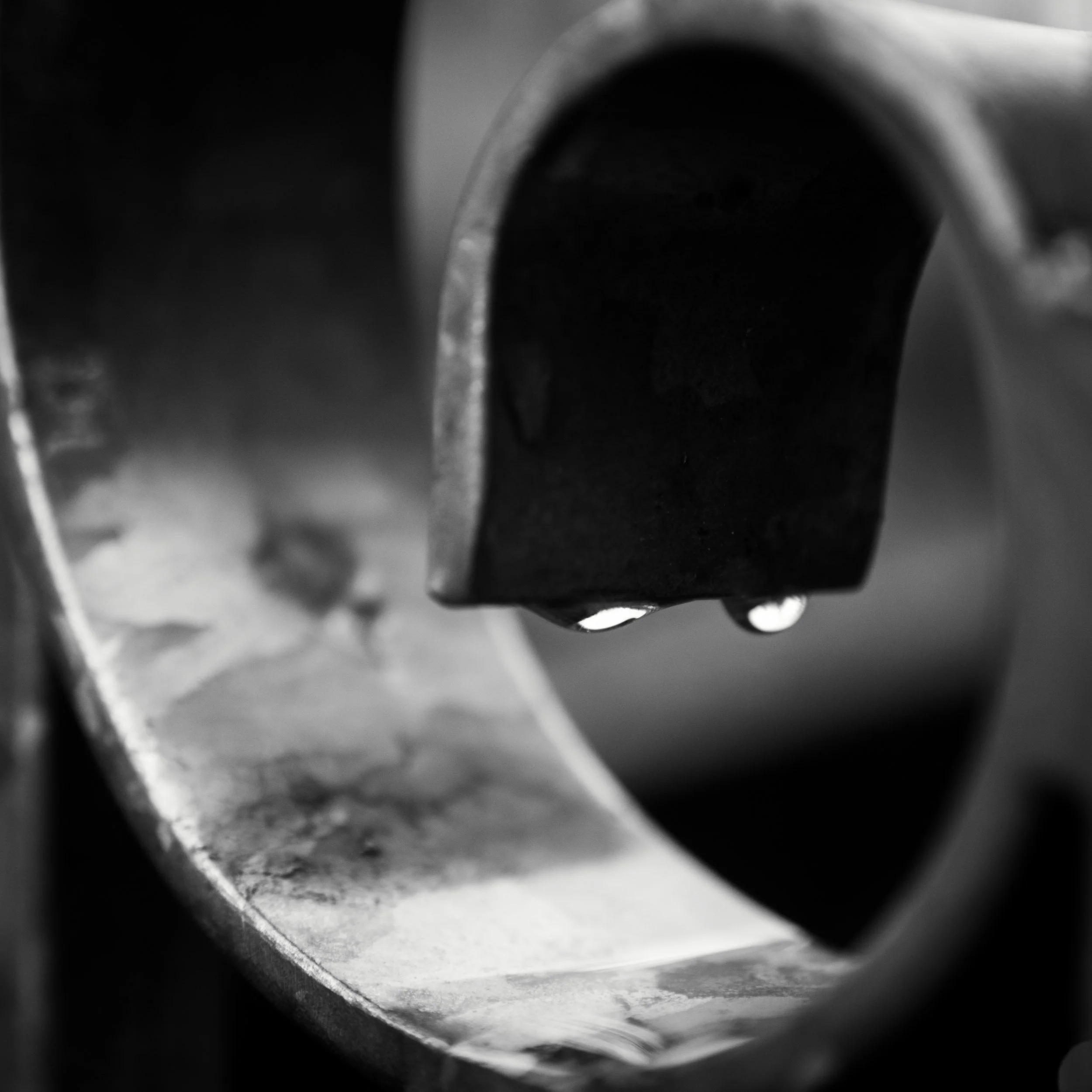 Black and white photograph of two water droplets hanging from curved metalwork railing.