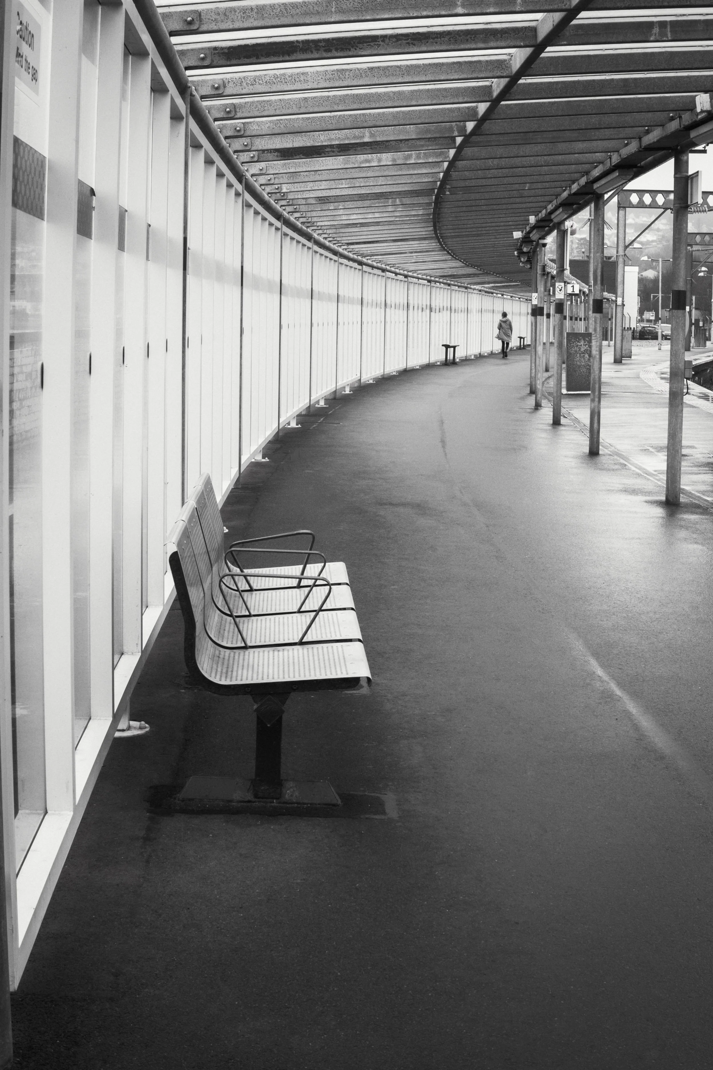 A dramatic monochrome capture of a quiet, modern train station platform walkway on a rainy day.