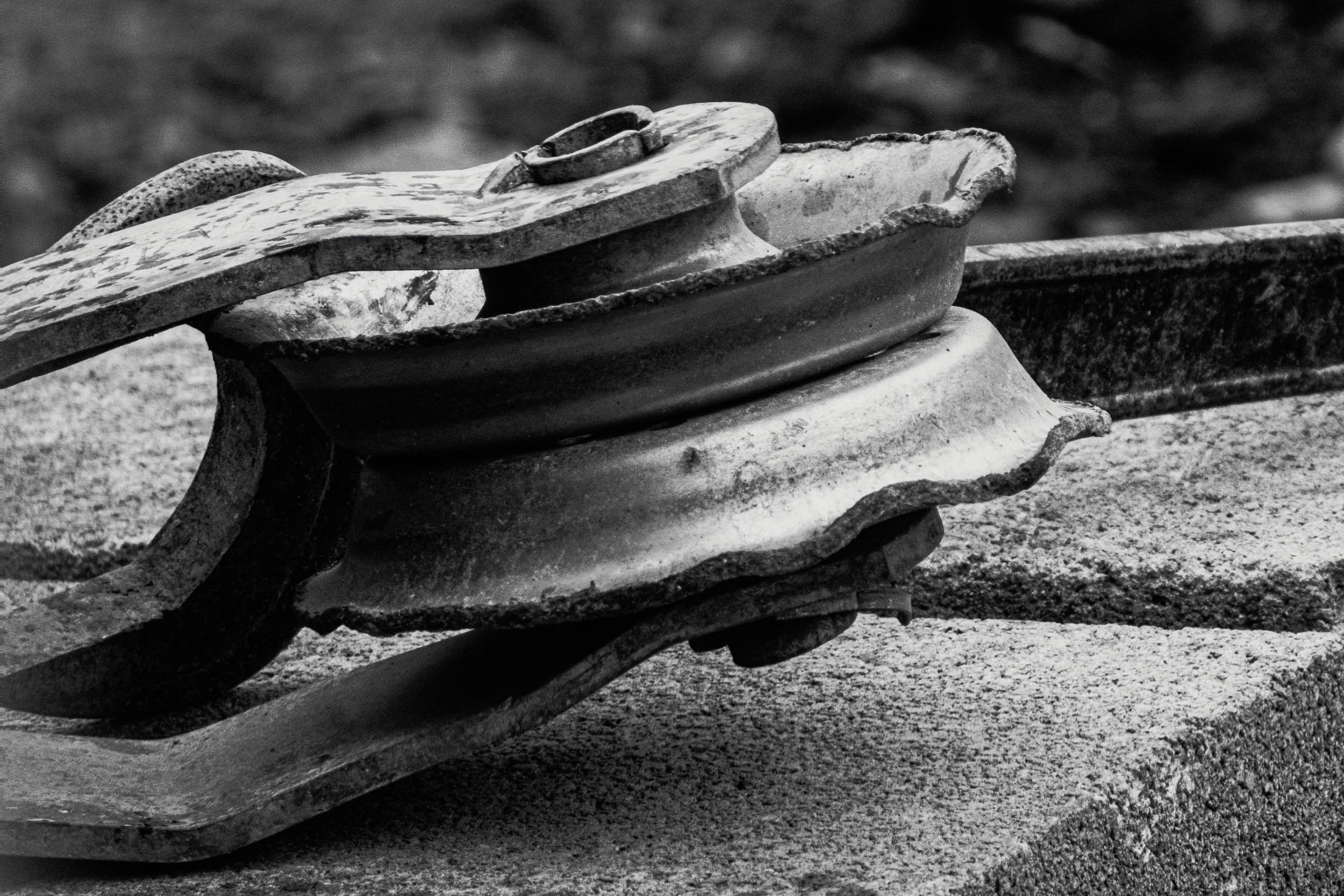 A heavy pulley with worn iron and rusted edges resting against cast concrete.