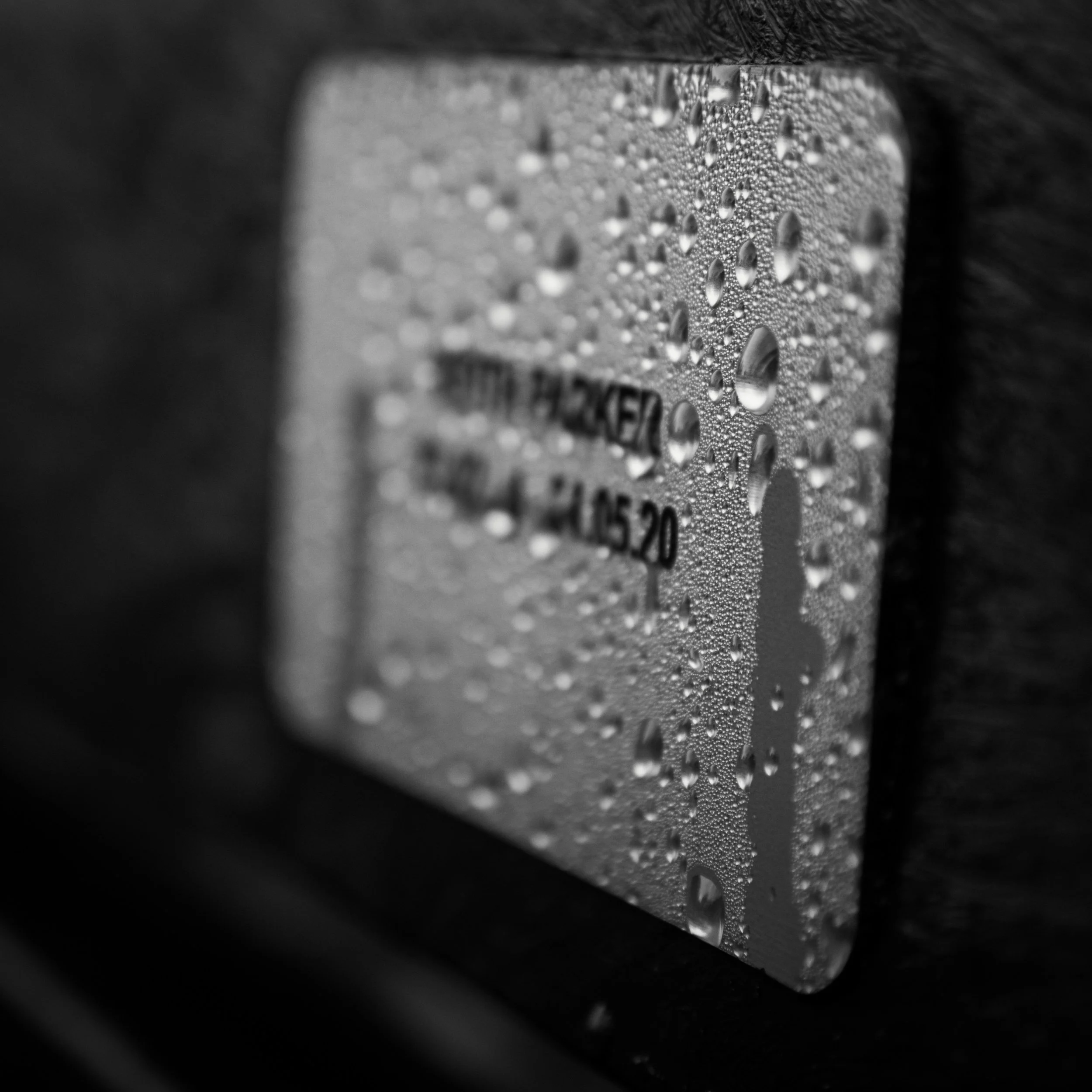 Close-up black and white photo of a rectangular card covered in fine water droplets and condensation.