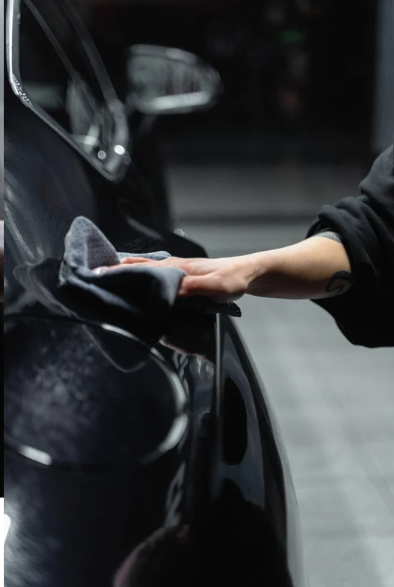 Une personne nettoyant la surface d'une voiture noire avec un chiffon.