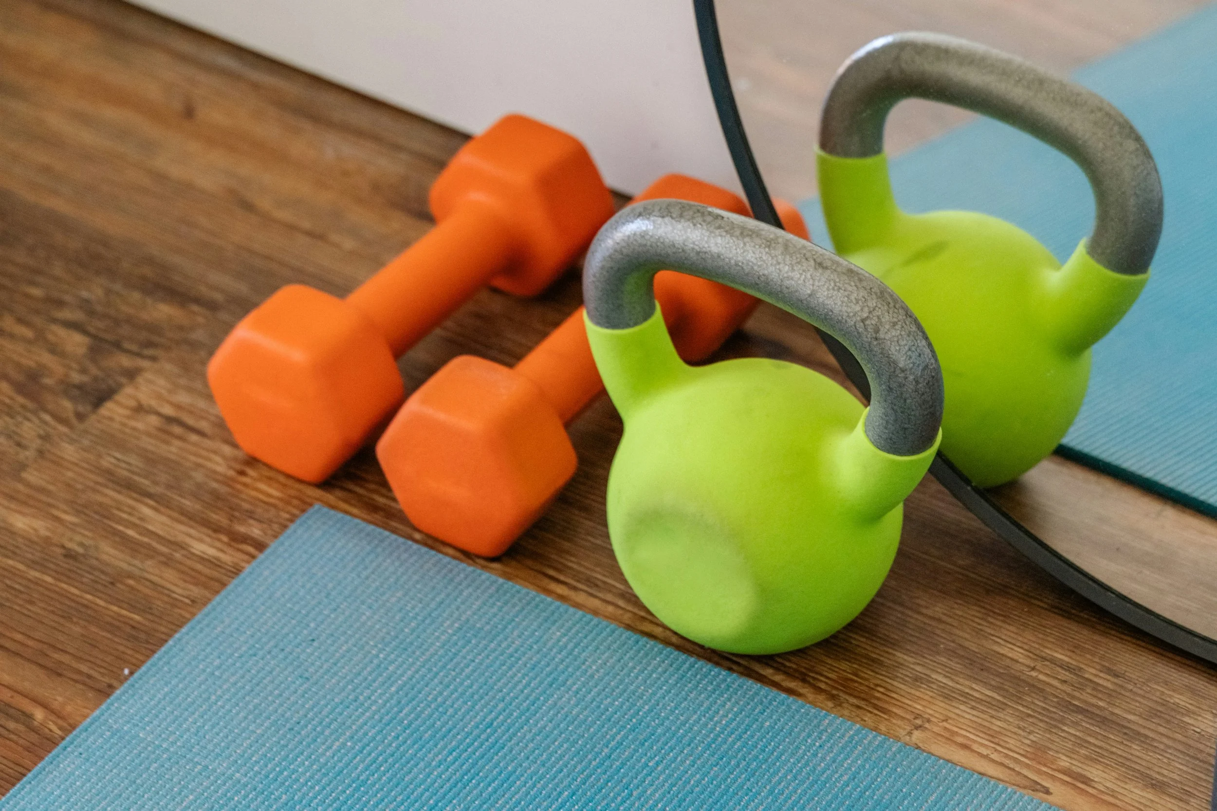 Set of orange dumbbells and green kettlebell on a wooden floor with yoga mats