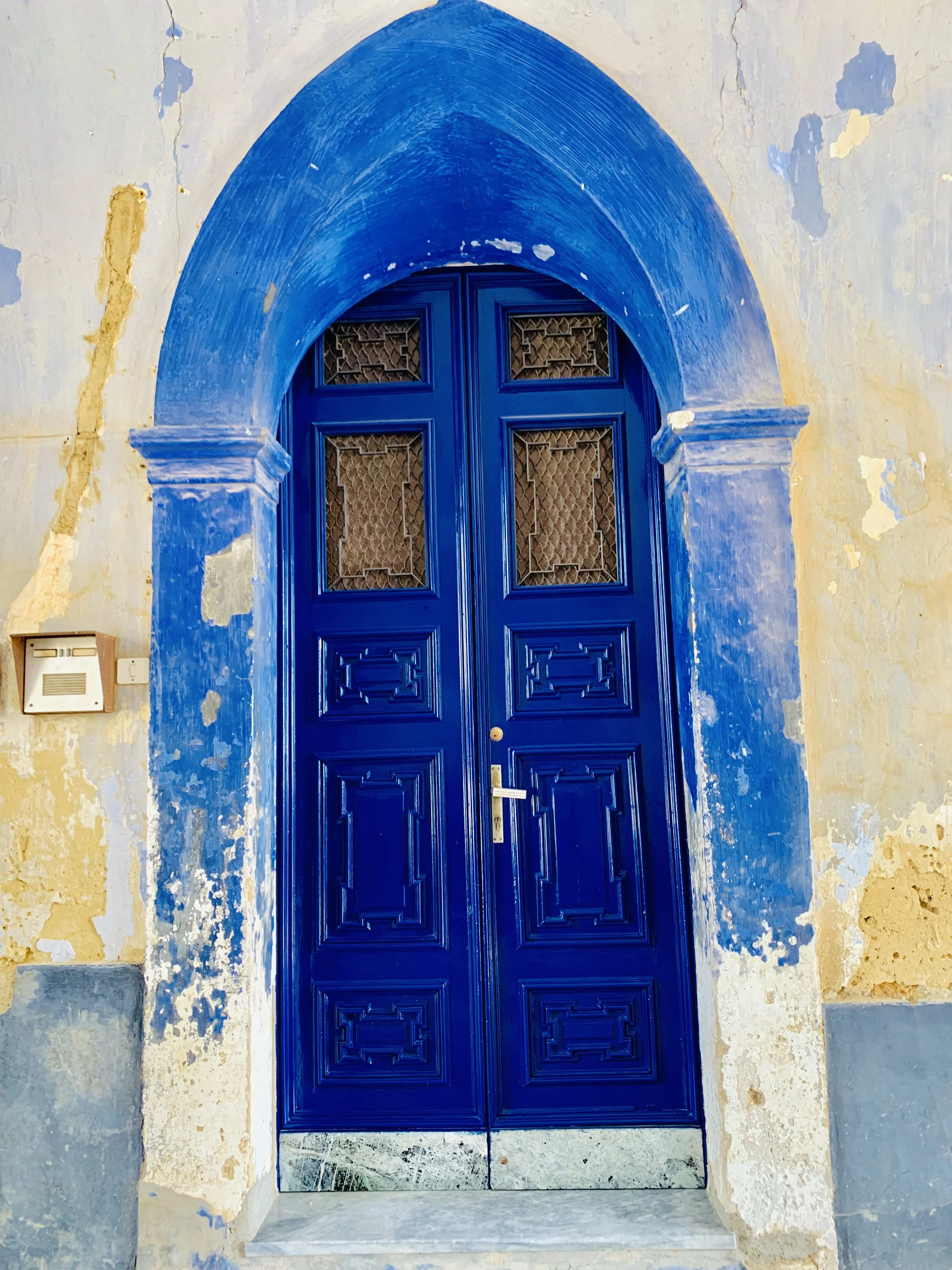 Blue arched door with decorative windows, set in a weathered wall with peeling paint.