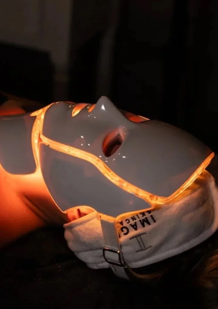 A person holding a broken ceramic face mask with glowing orange edges in a dark environment.