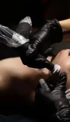A person receiving a tattoo from a tattoo artist wearing black gloves.
