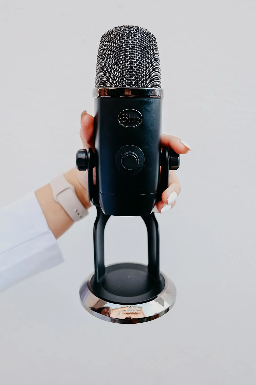 A person holding a black Blue microphone with a silver grille against a white background.