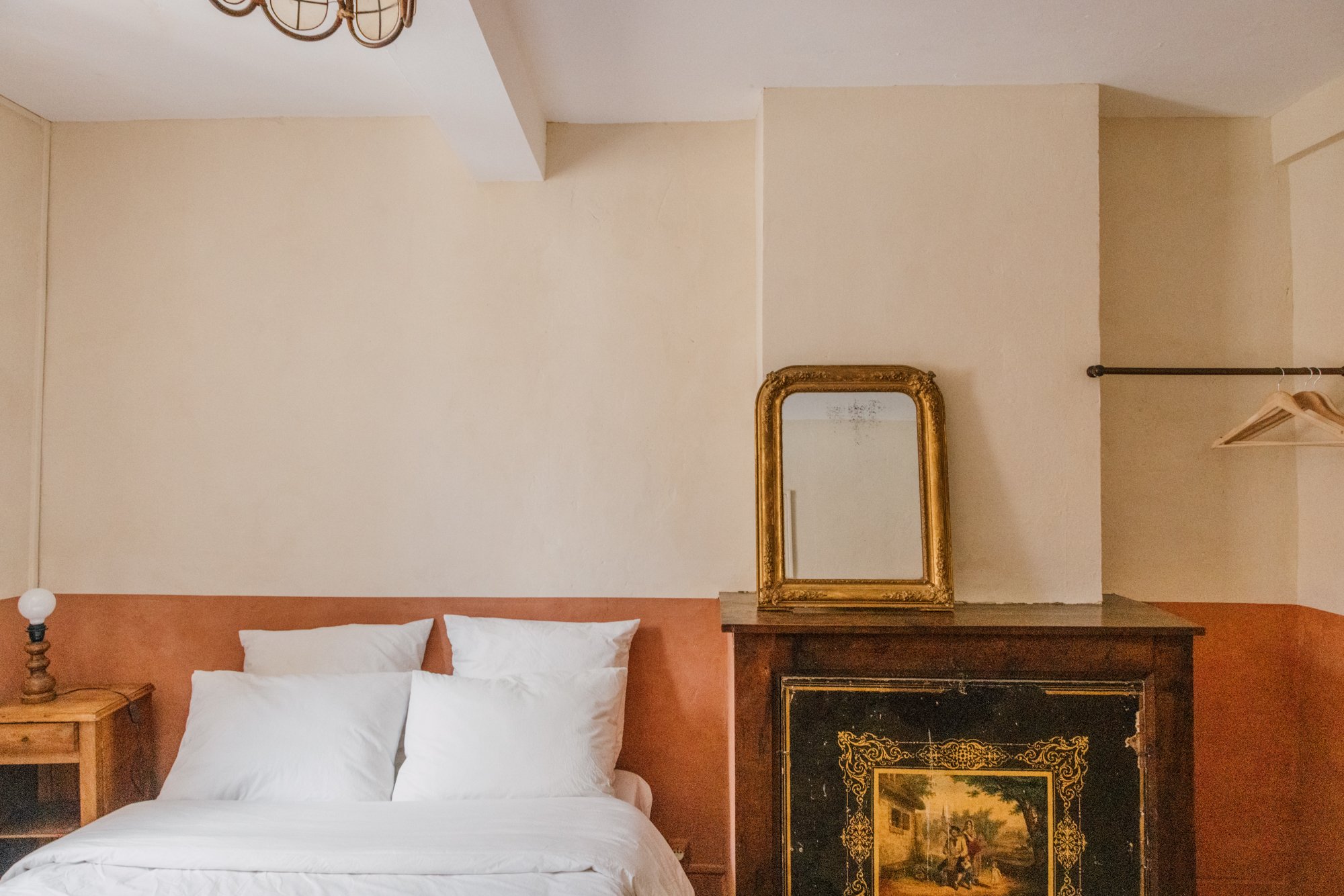 Chambre avec lit blanc, miroir doré et cheminée ancienne décorée