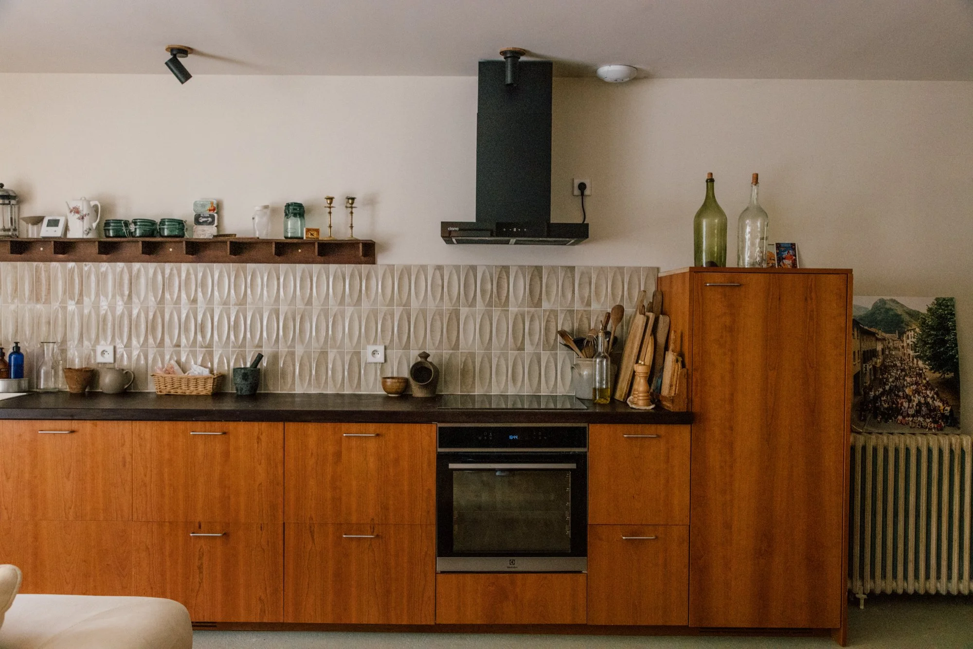 Cuisine avec armoires en bois, plan de travail noir, cheminée en noir, grille de ventillation, ustensiles et décorations