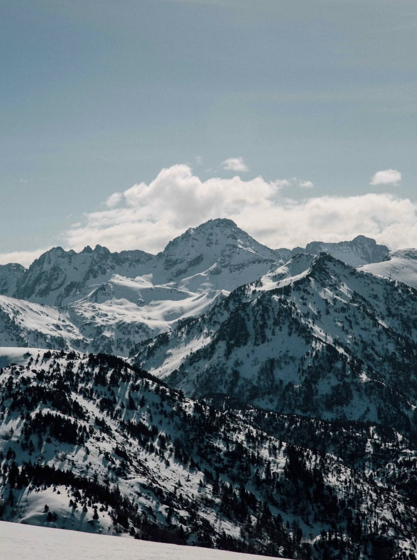 Chaîne de montagnes enneigées avec ciel bleu et quelques nuages.