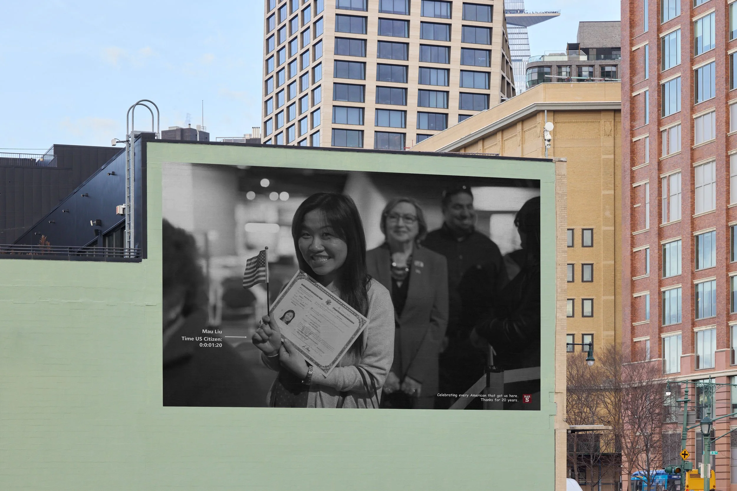 A large black-and-white photograph on a green building shows a young woman smiling and holding a passport, American flag, and a certificate, with three people in the background. The caption indicates she is Mau Liu, celebrating her citizenship. Modern city buildings are visible in the background.
