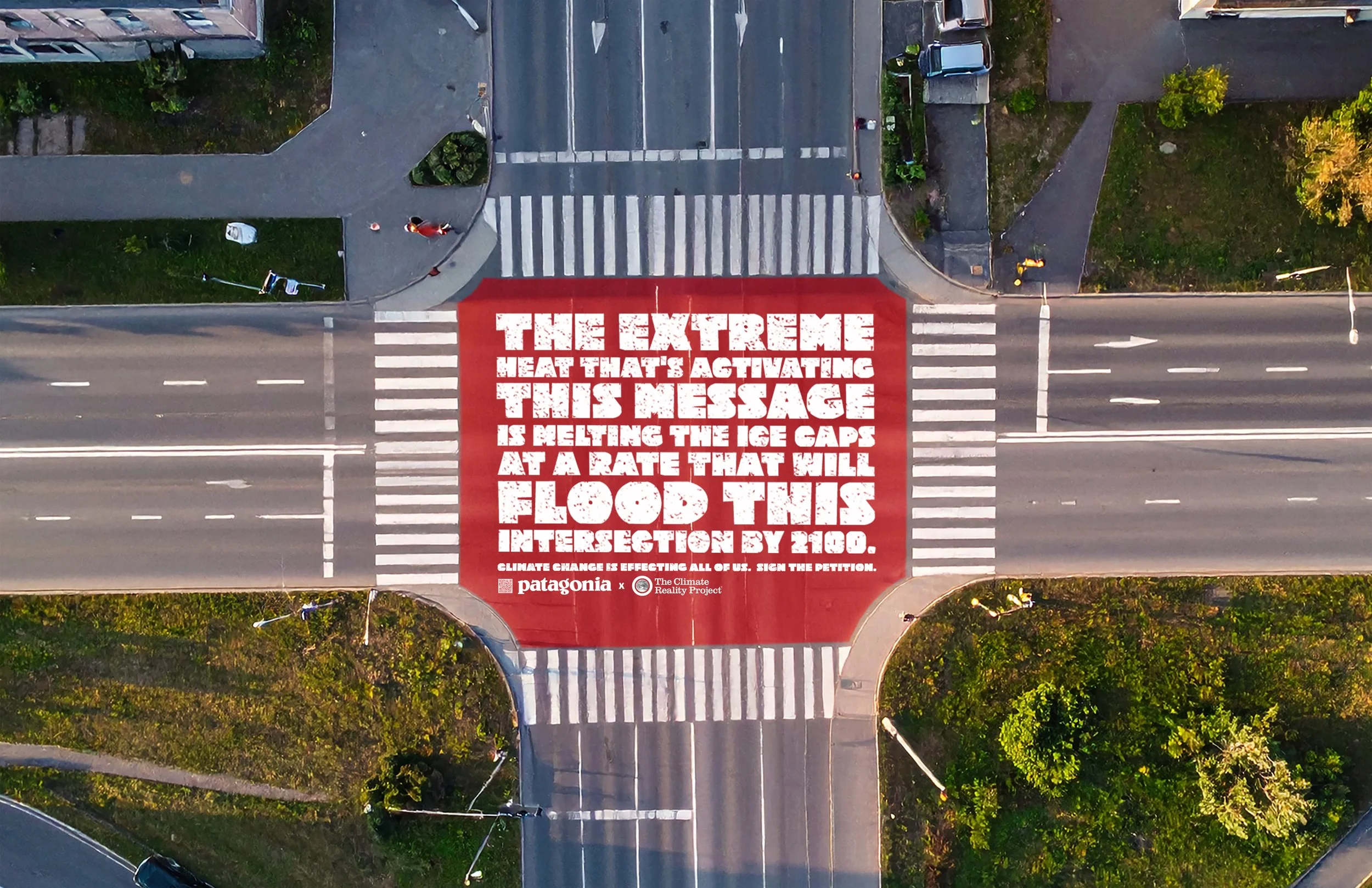 Aerial view of a crosswalk painted over a road with a red message saying 'The extreme heat that's activating this message is melting the ice caps at a rate that will flood this intersection by 2100.'