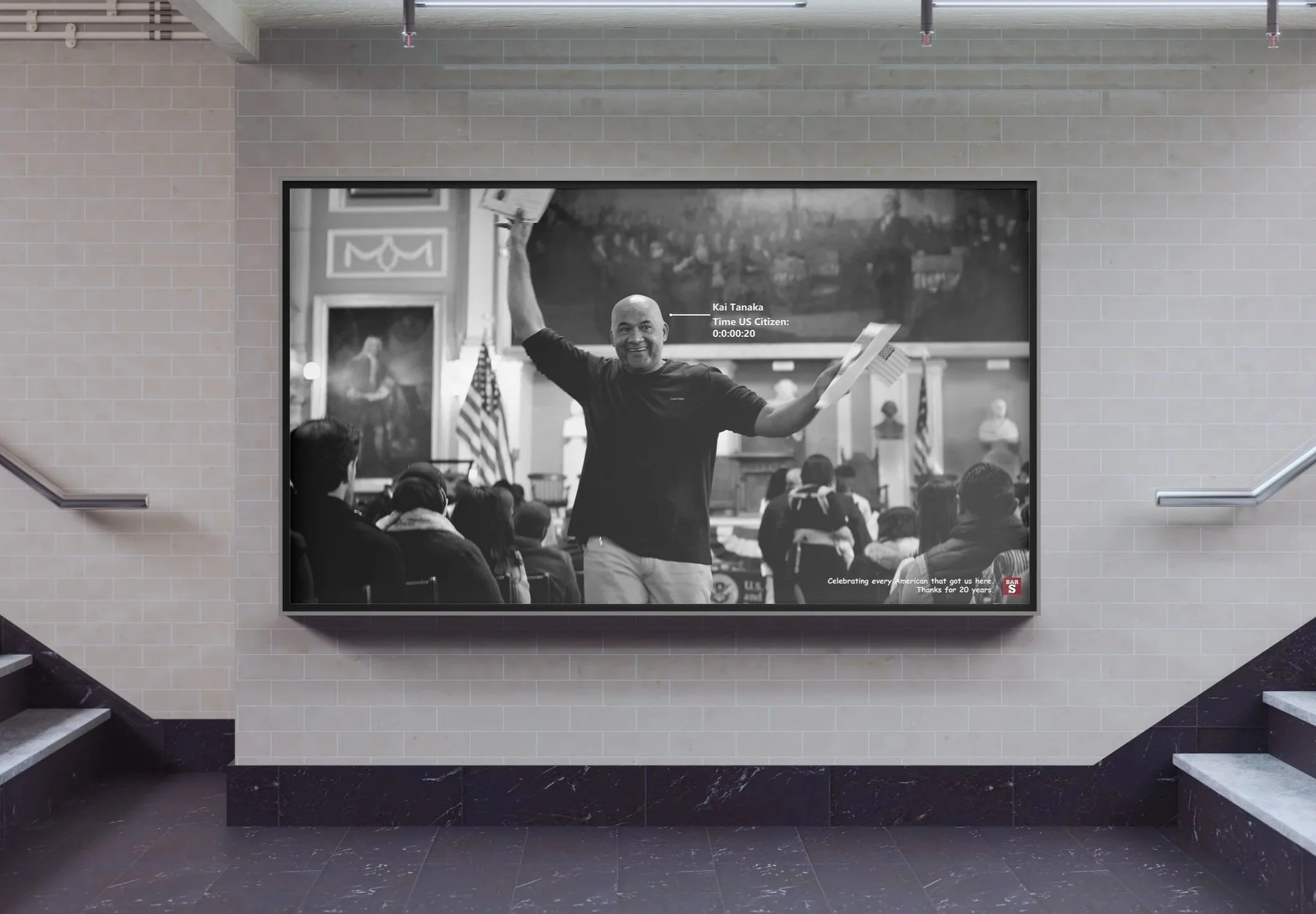 Black-and-white photograph of a man in a room with an American flag, standing with arms raised, for a celebration or event, with an audience seated and a large portrait painting visible in the background.