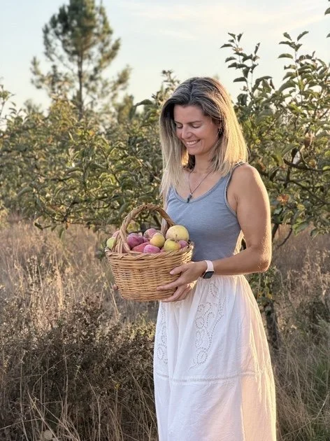 Mulher sorridente segurando uma cesta de maçãs em um campo ao ar livre.