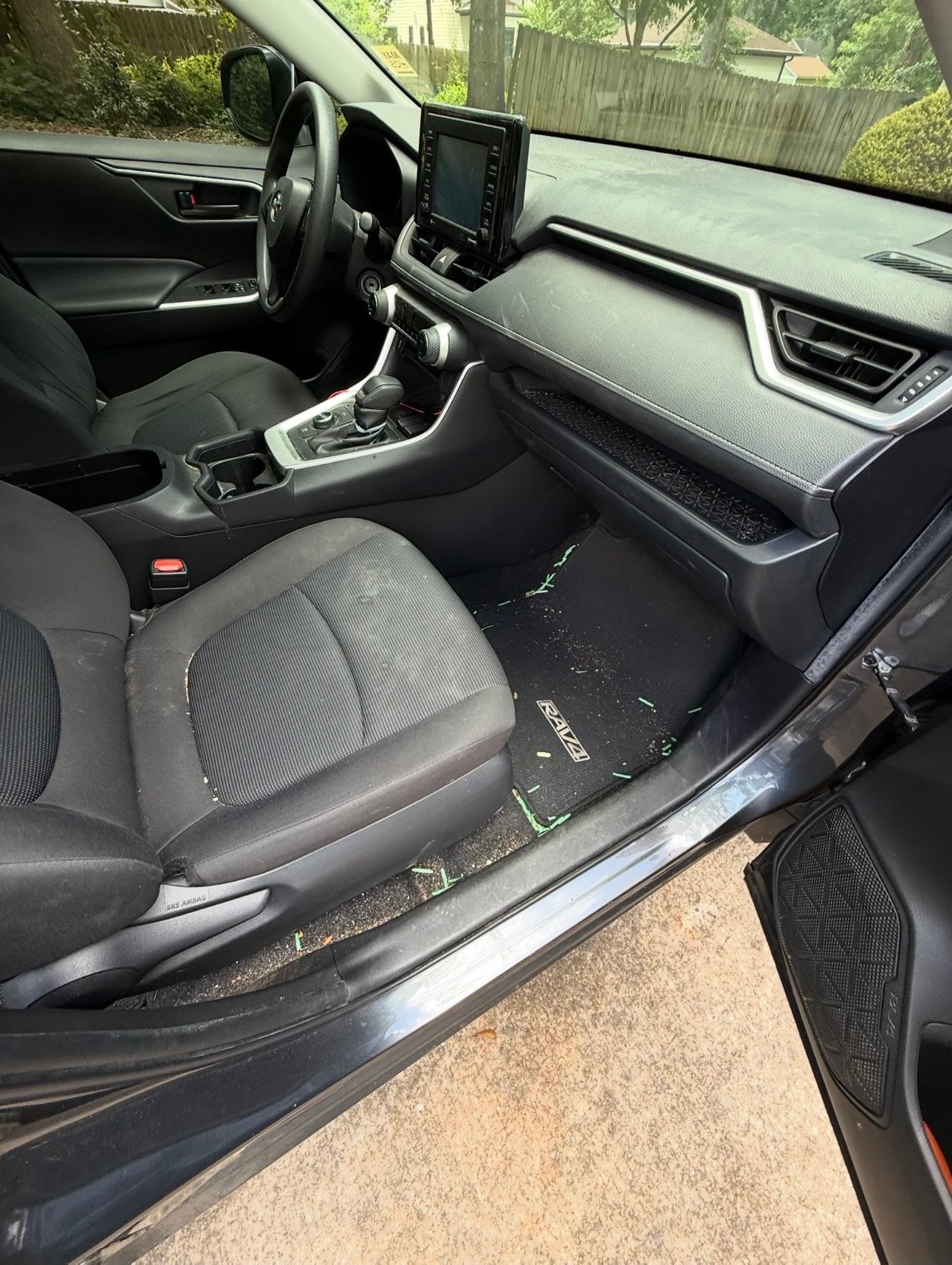 Interior of a black Toyota vehicle showing the front seats, dashboard, and center console. The driver's seat has some dirt and debris on the floor mat.