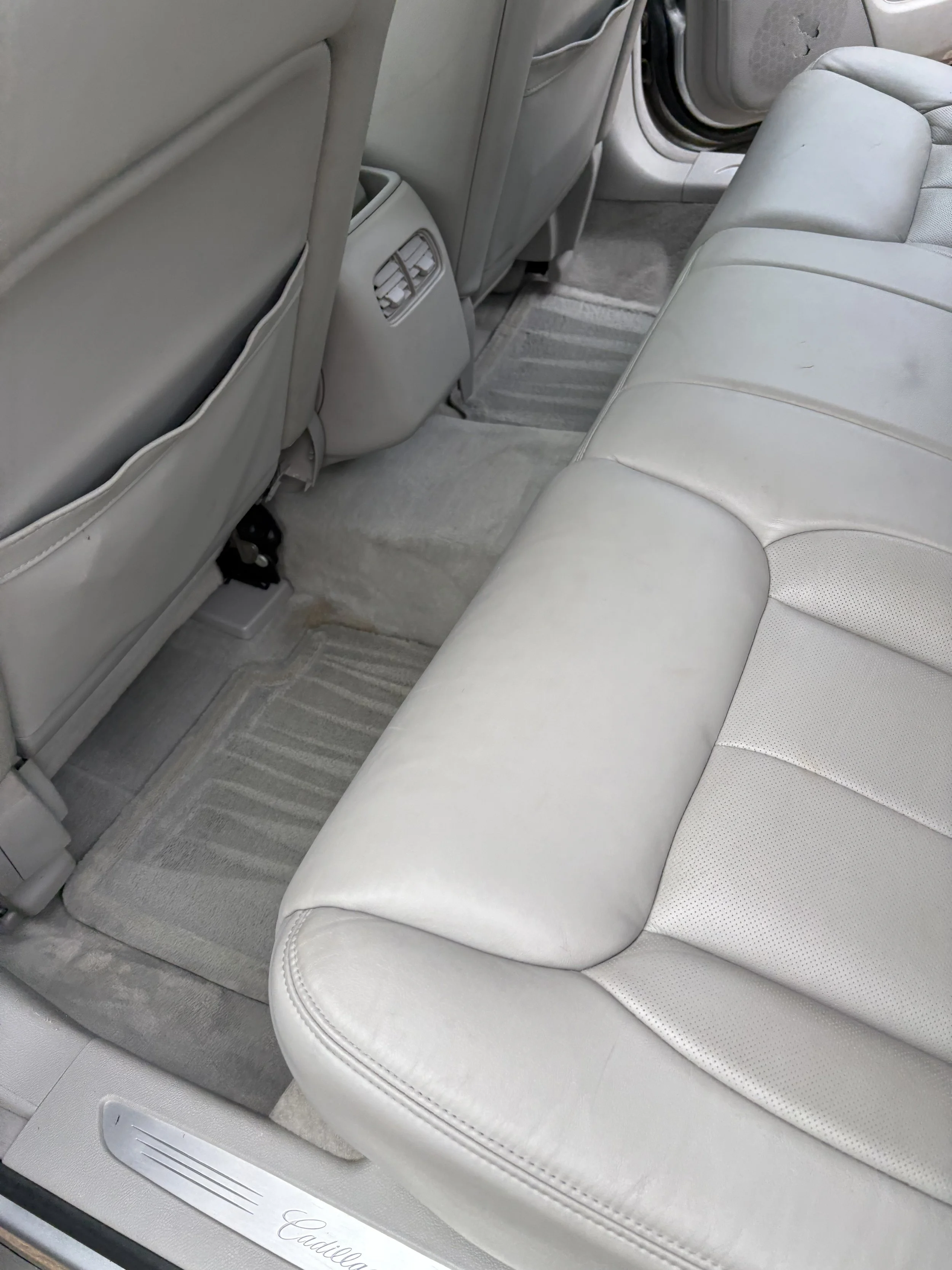 The back seat area of a light gray car interior, featuring a three-quarter leather seat and a gray carpeted floor with matching floor mats.