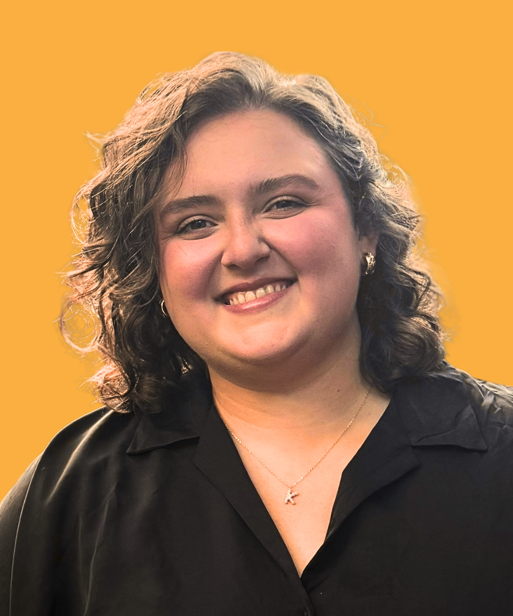 A woman with curly hair smiling, wearing a black shirt, against a yellow background.