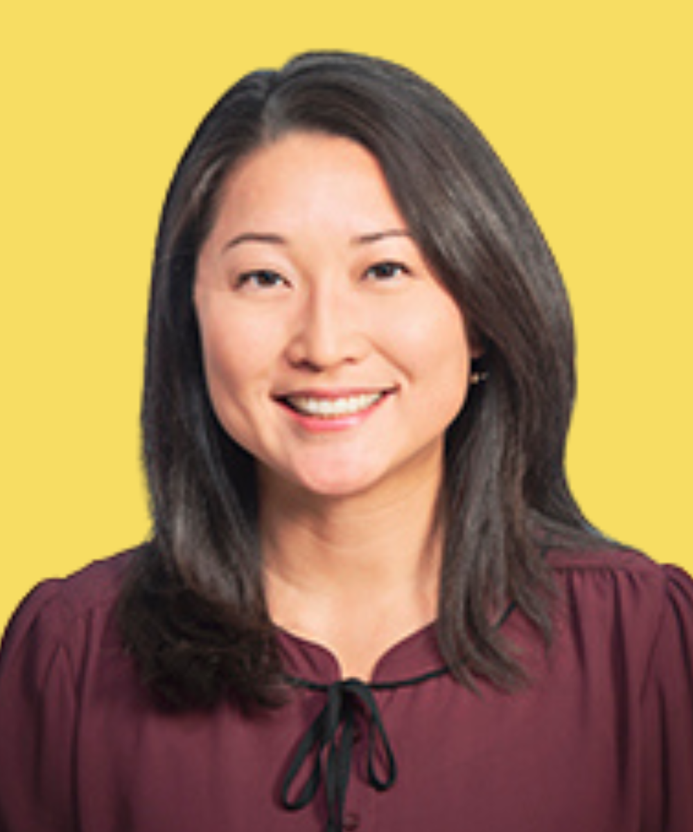 A woman with shoulder-length dark hair, smiling, wearing a maroon blouse, against a yellow background.
