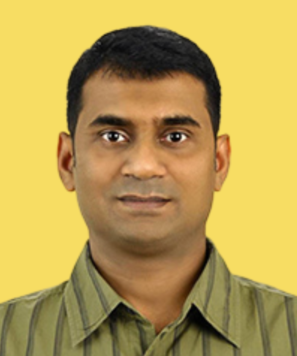 Portrait of a man with short black hair, wearing a green striped collared shirt, against a yellow background.