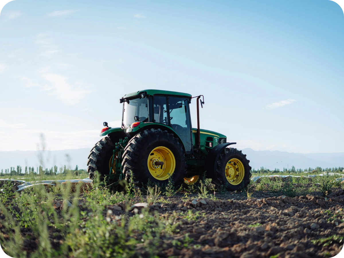 Green tractor working in a farm field under a blue sky.