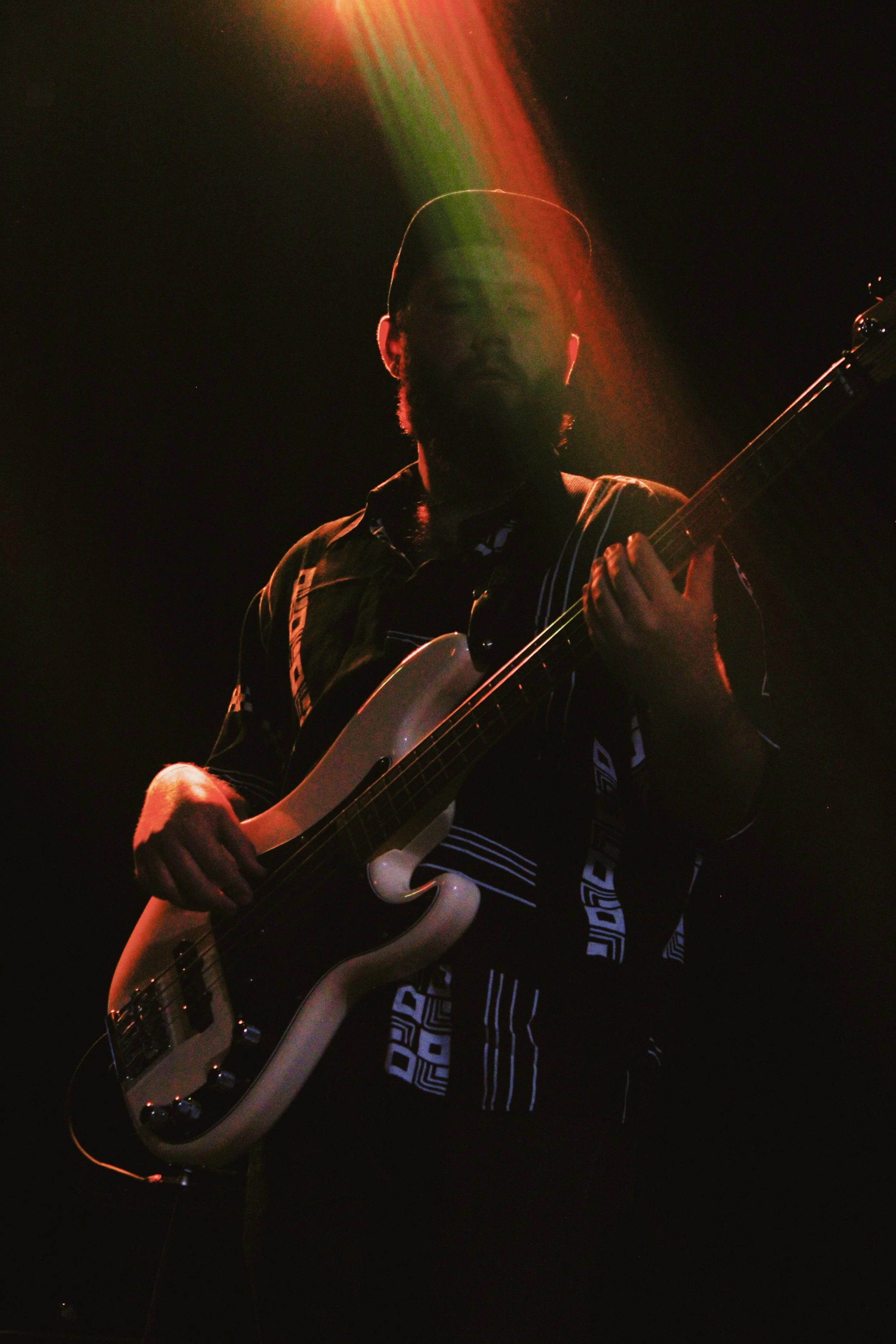 Person playing electric bass guitar on stage with stage lighting creating a colorful light streak.
