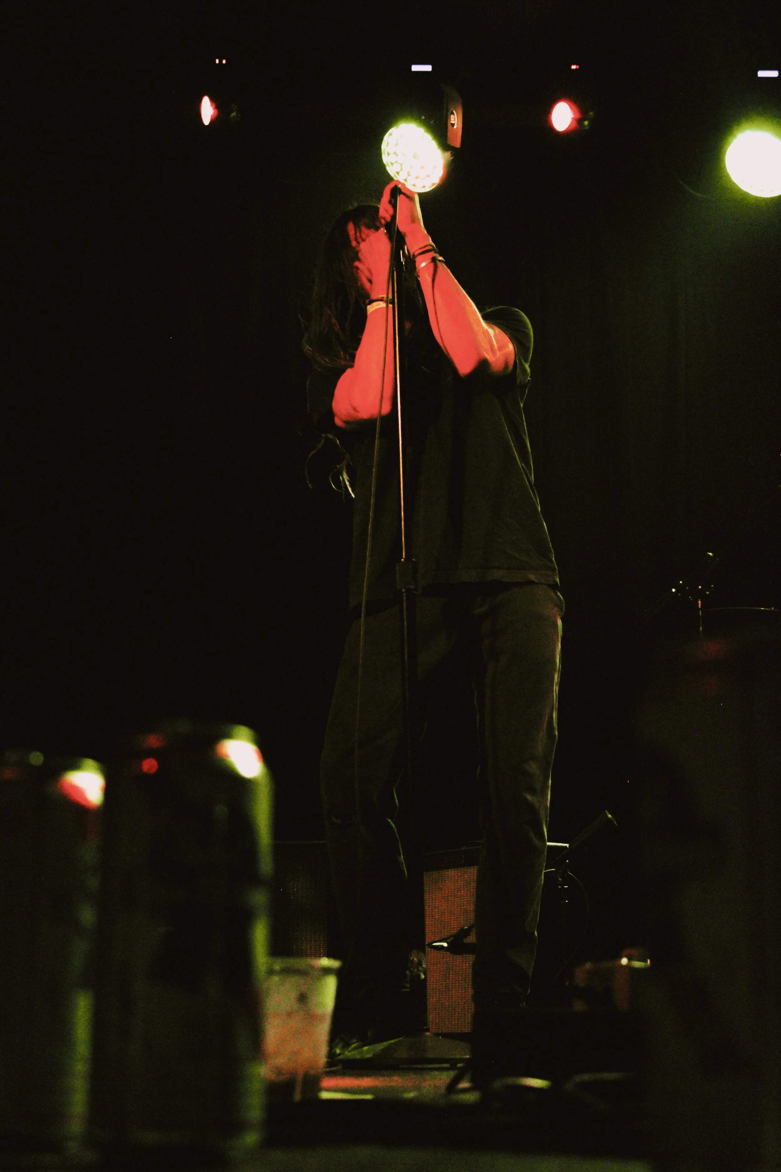 A singer on stage holding a microphone with stage lights overhead.