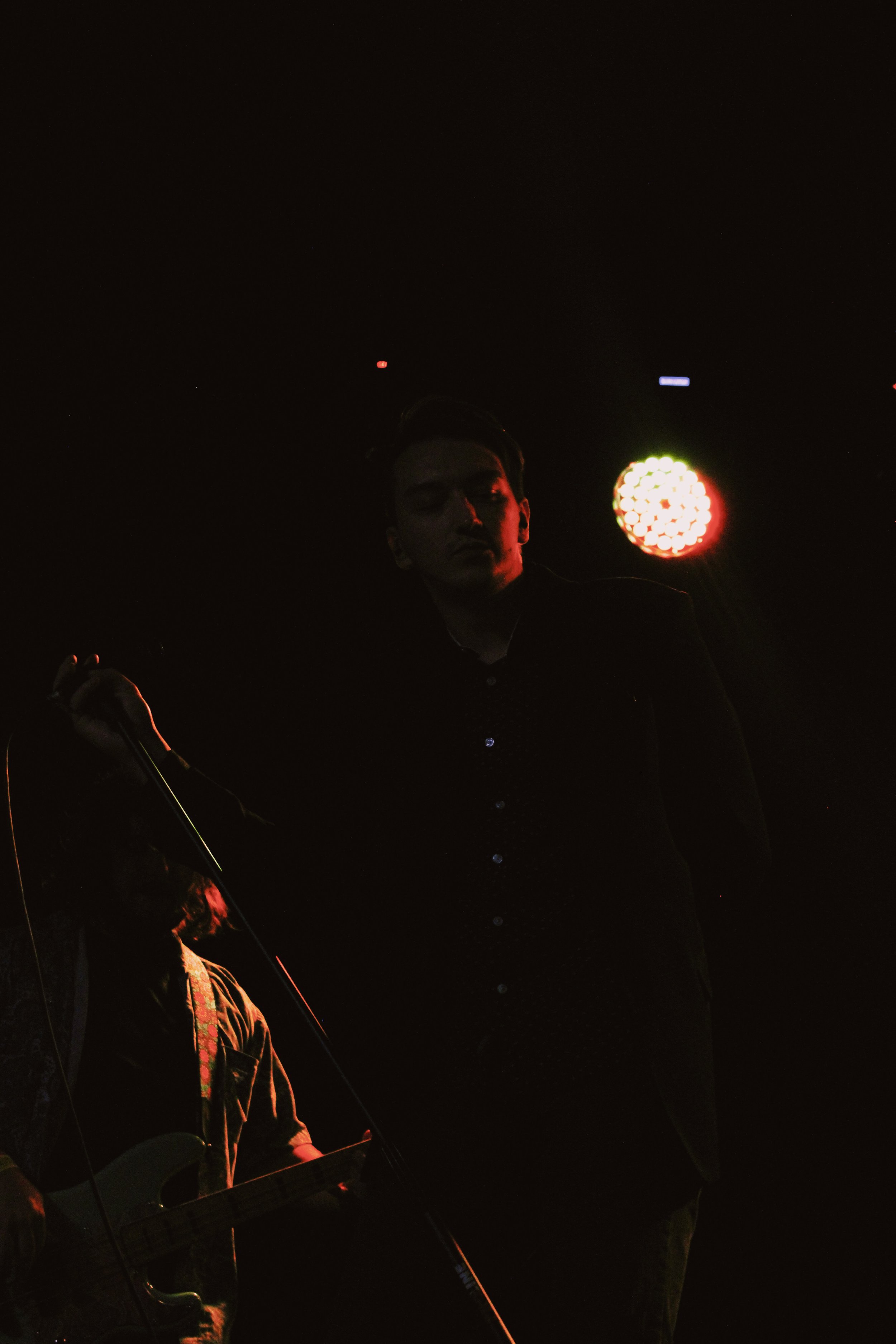 A singer performing on stage with a guitarist, illuminated by stage lights at night.