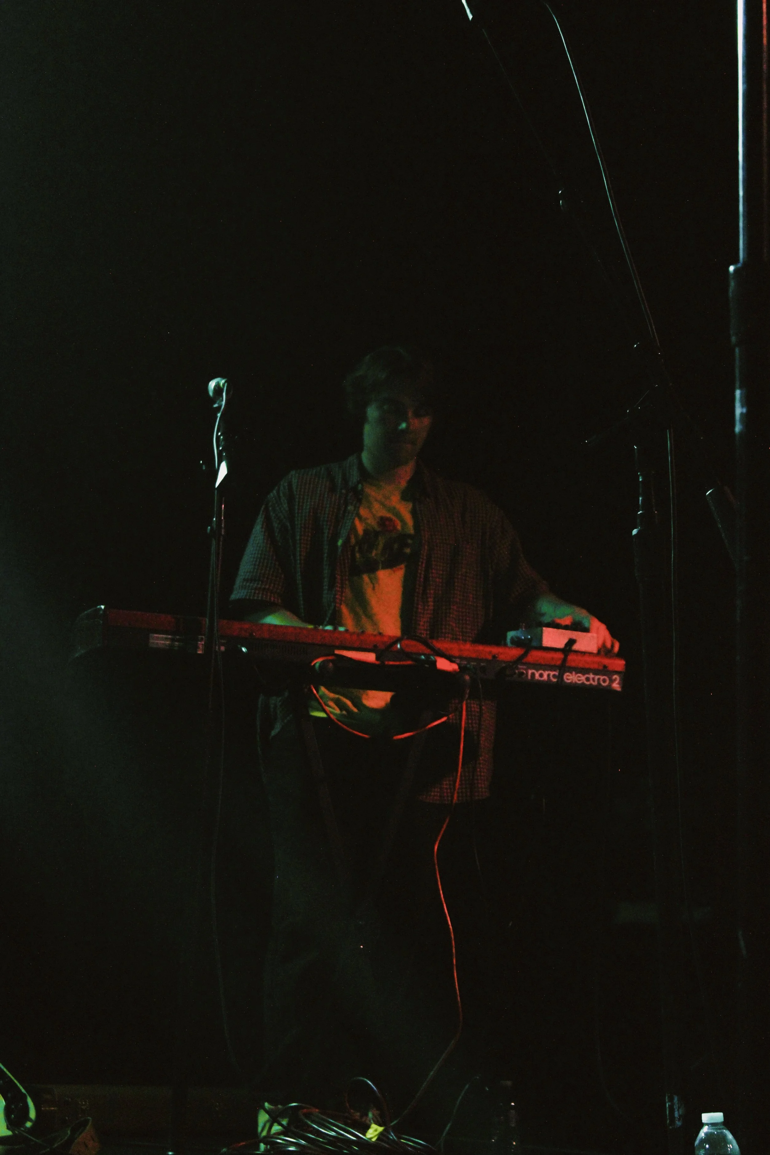 A person playing a keyboard on stage in a dark setting.