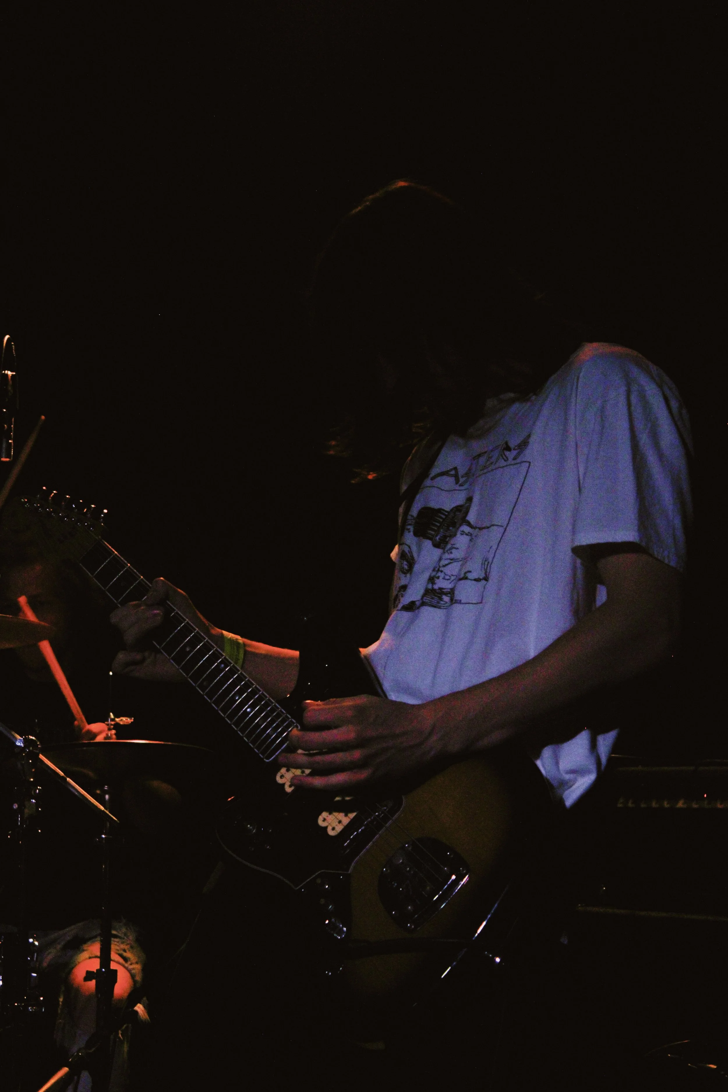 Person playing an electric guitar on stage against a dark background.