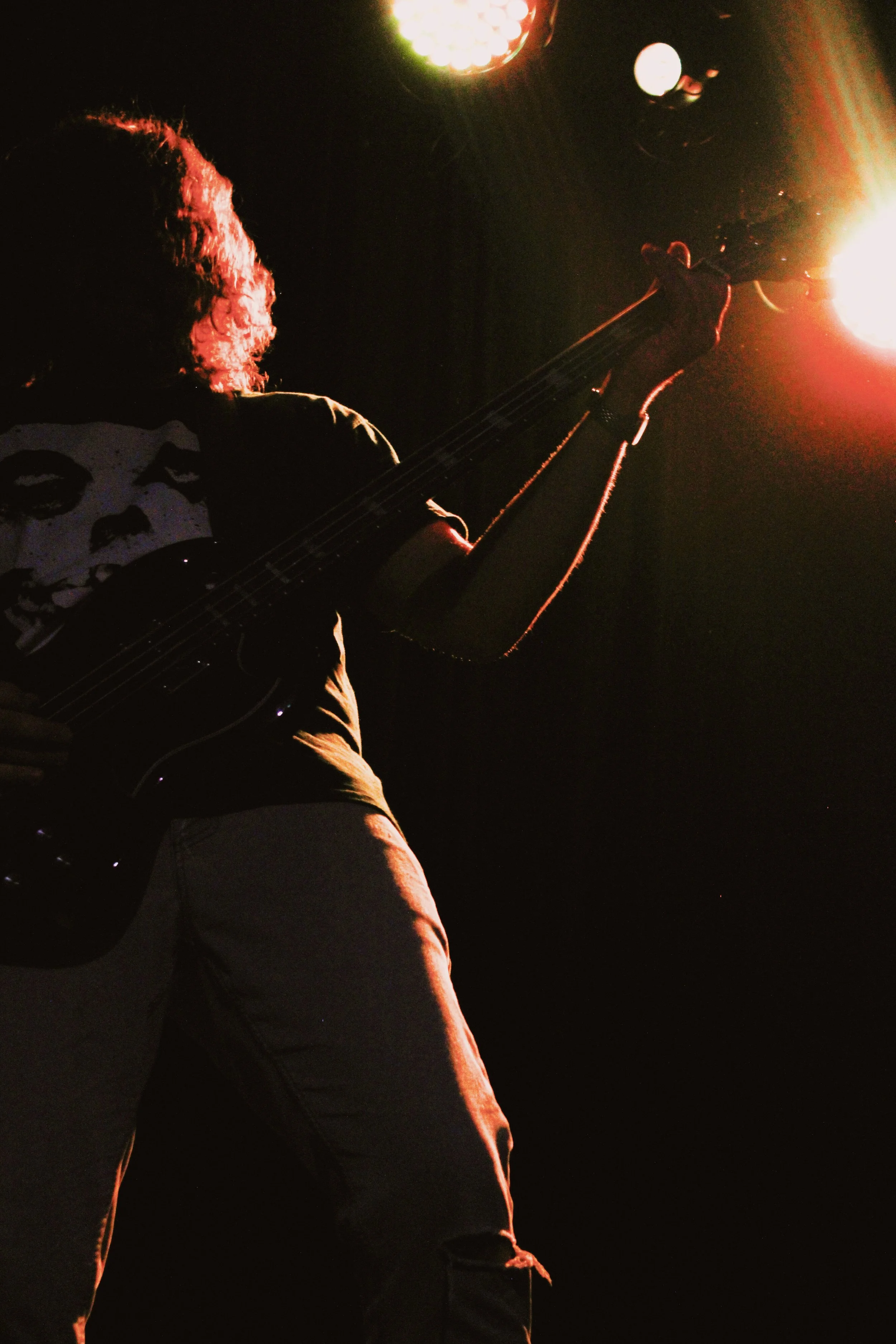 A silhouette of a person playing an electric guitar on stage during a performance at night, with bright stage lights.
