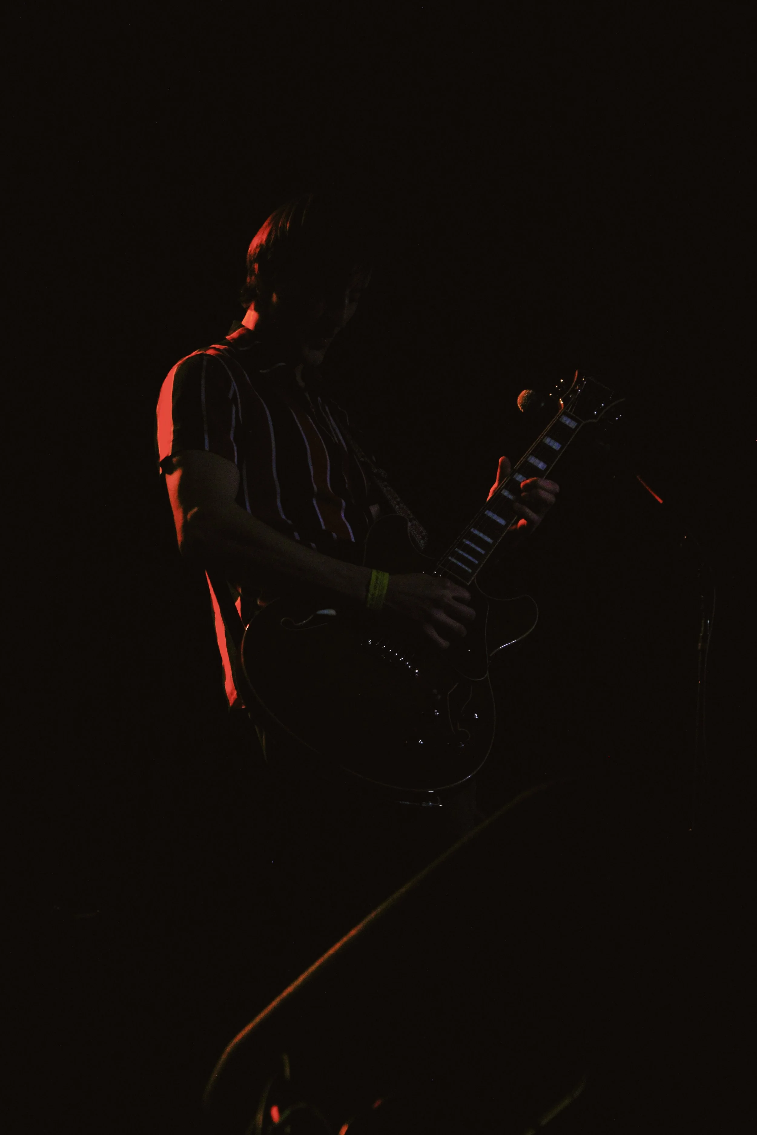 Silhouette of a musician playing an electric guitar on stage in low light.