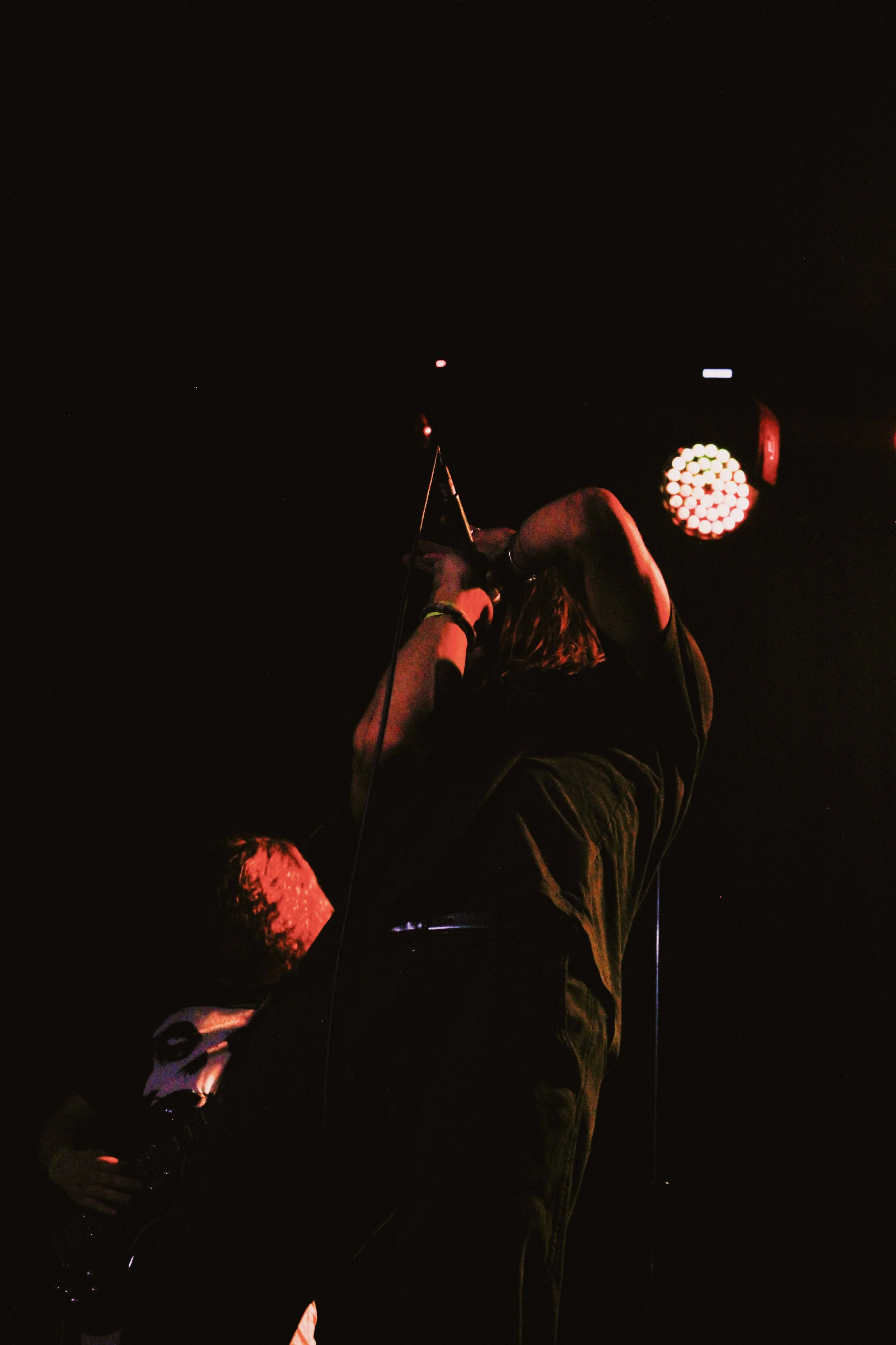 Musician singing into a microphone on stage with stage lighting.