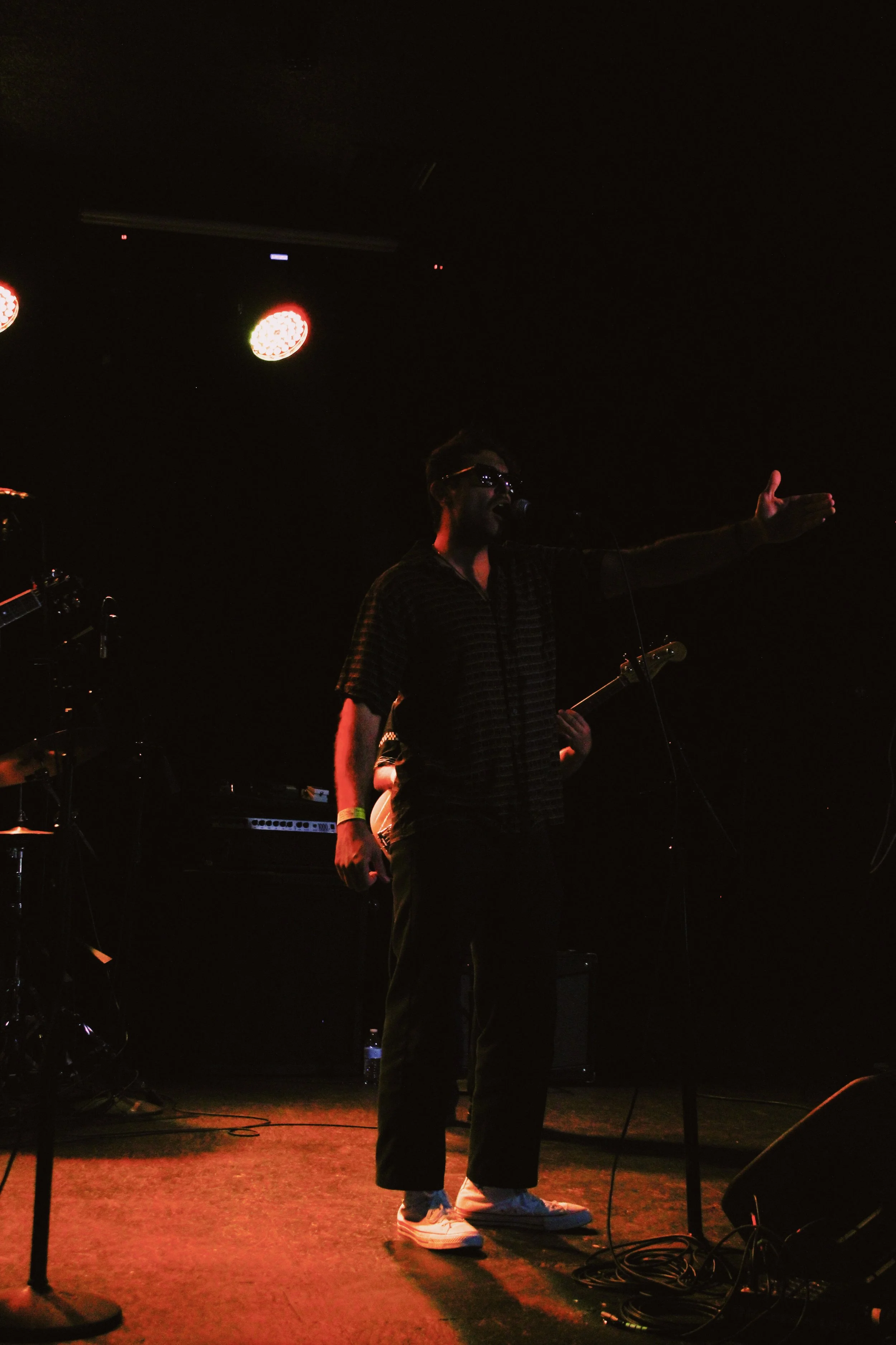 A person performing on stage with a microphone, in a dark setting with stage lights overhead.