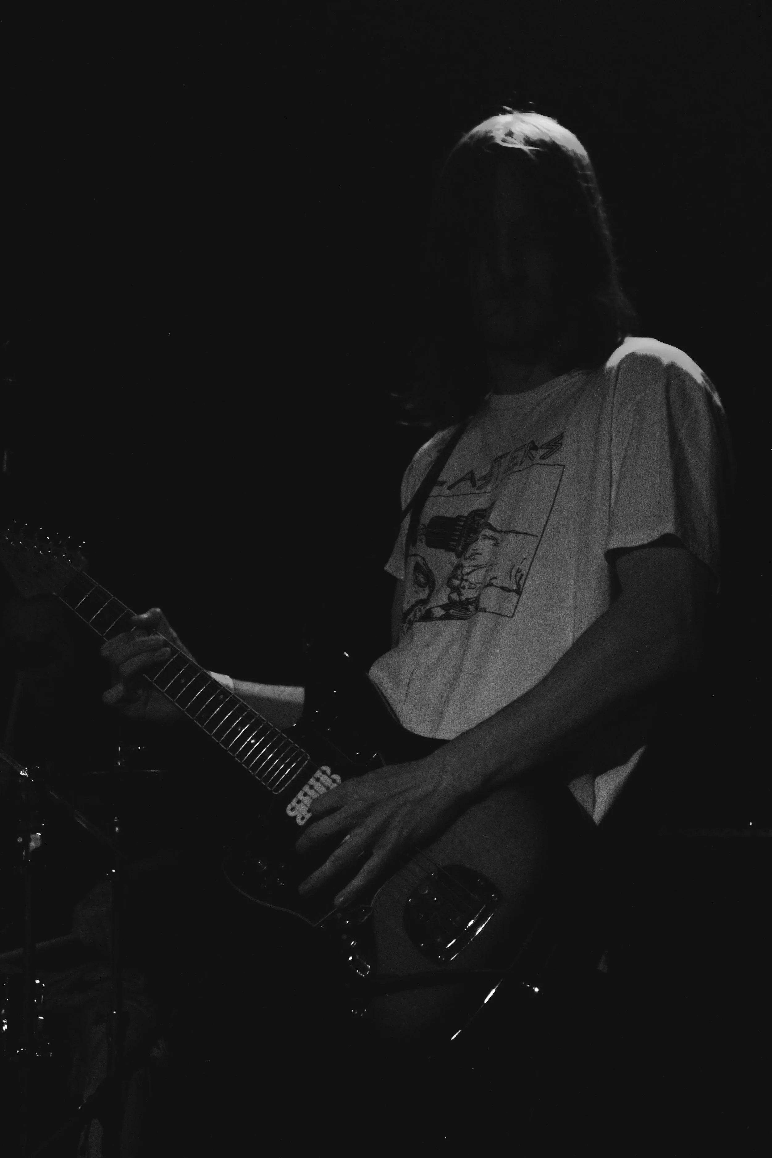 A person playing an electric guitar in a dark setting, wearing a T-shirt with a graphic design.