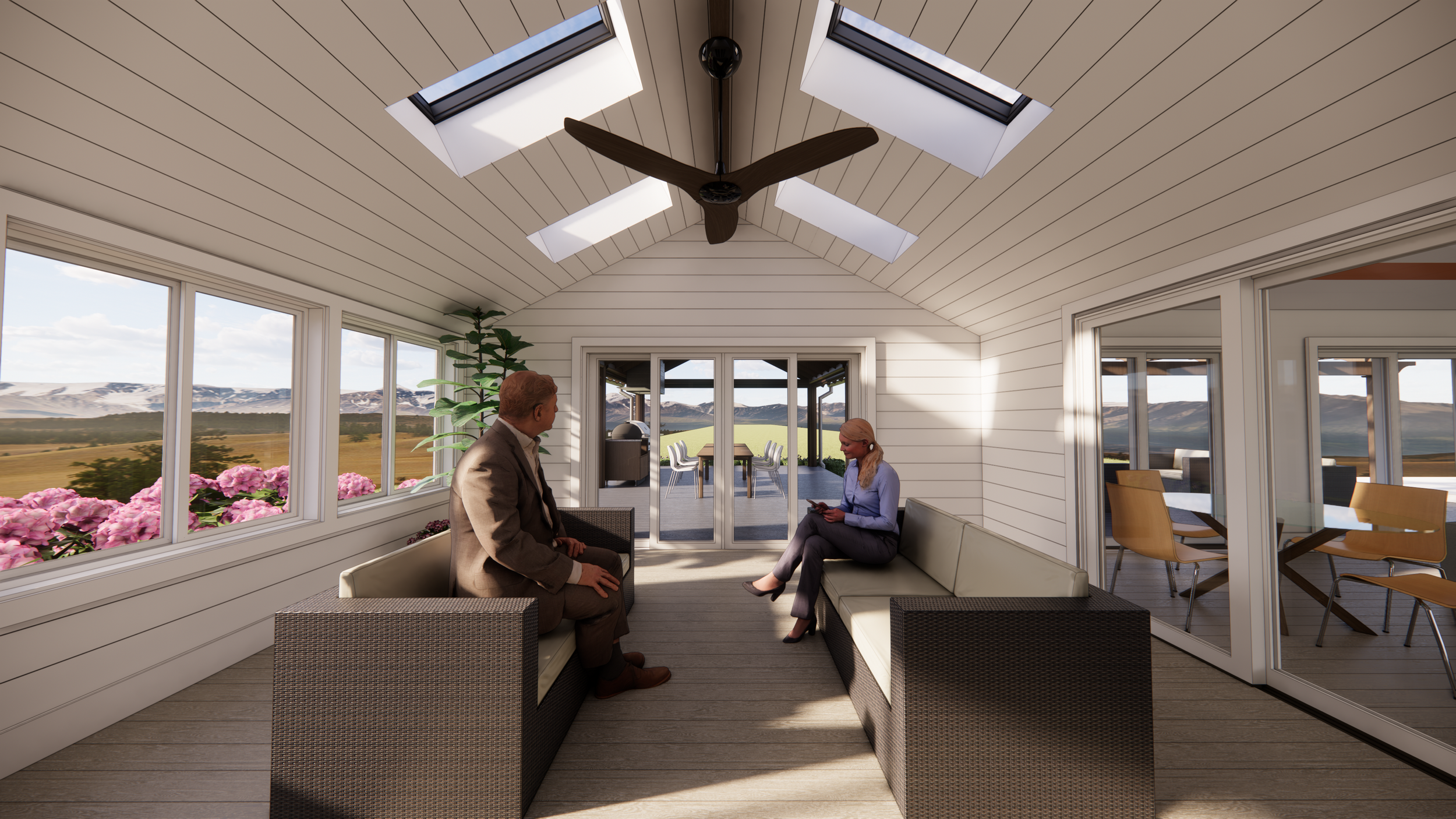 A spacious enclosed porch with two people sitting and engaging in conversation, surrounded by large windows with a view of landscape with mountains and fields, and a balcony with outdoor furniture.