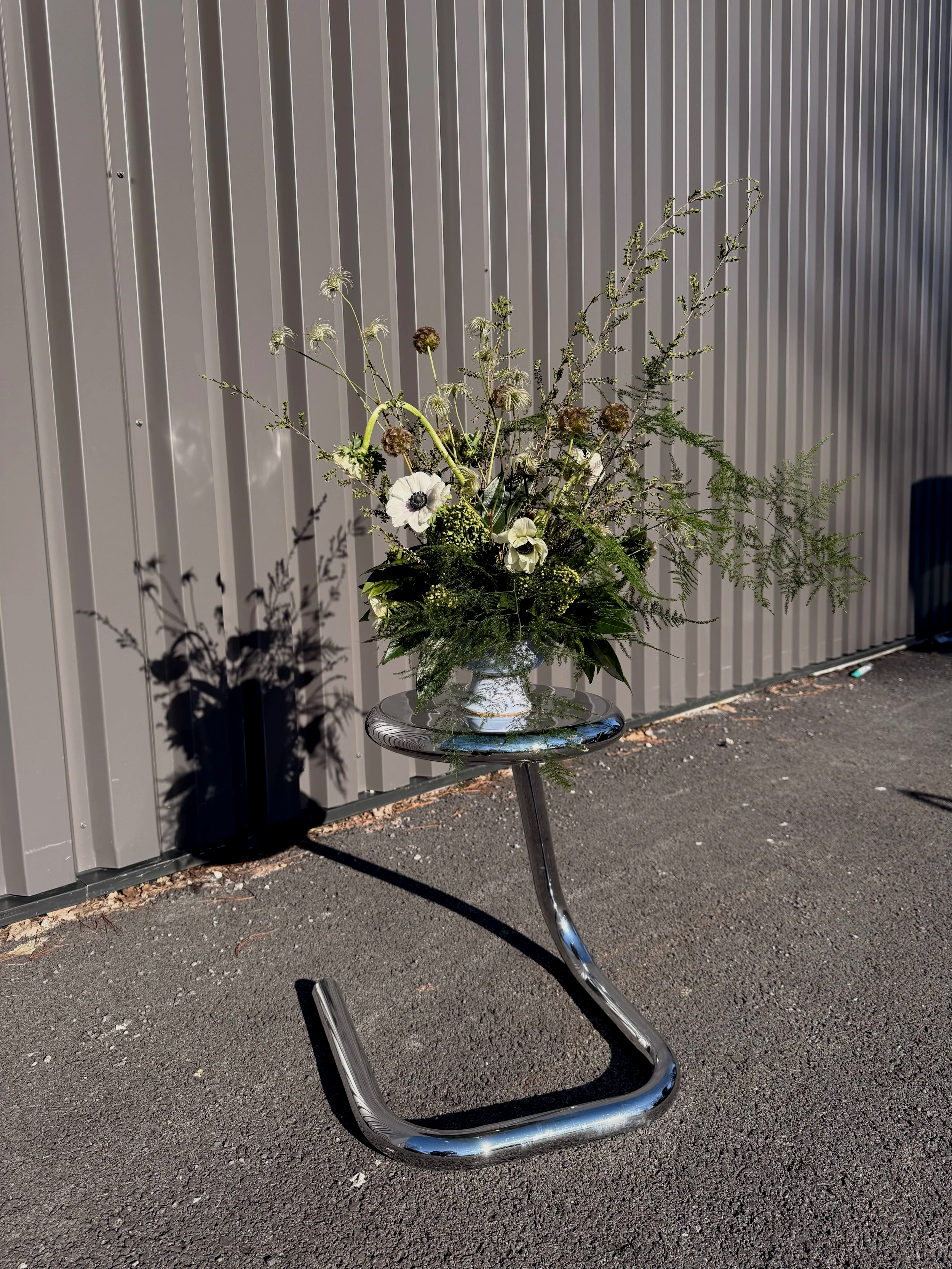 Un bouquet de fleurs sans vase posé sur un guéridon en métal dans un espace extérieur